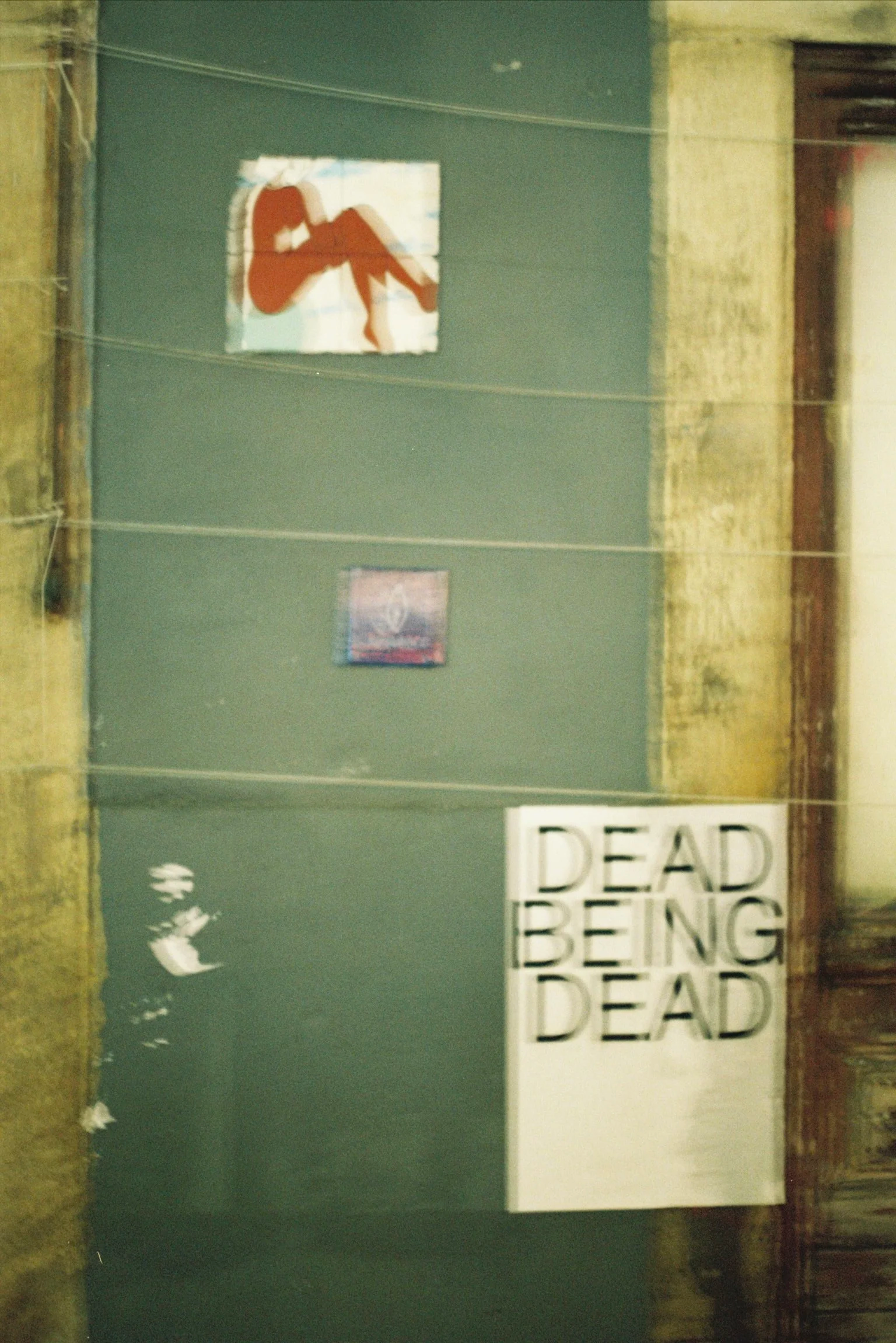 A wall with posters and text, including one large sign reading 'DEAD ENDING' with black letters on white background. One poster features a silhouette of a woman sitting with her legs crossed.