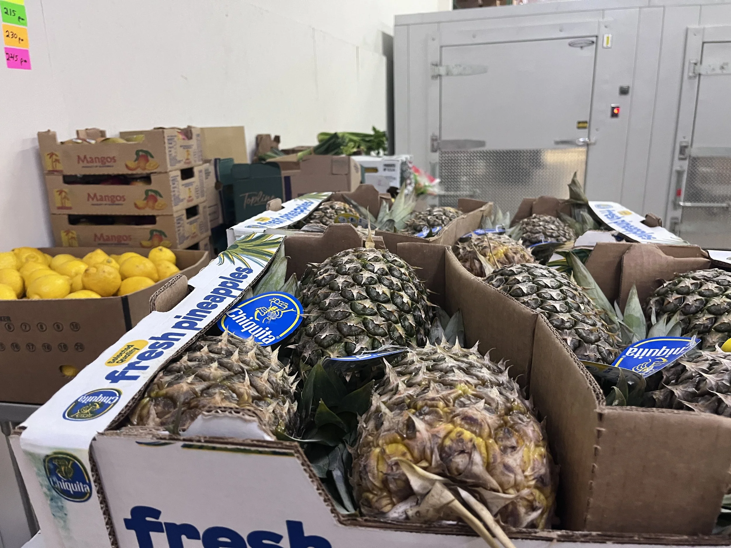 Fresh pineapples and lemons displayed in boxes on a store shelf.