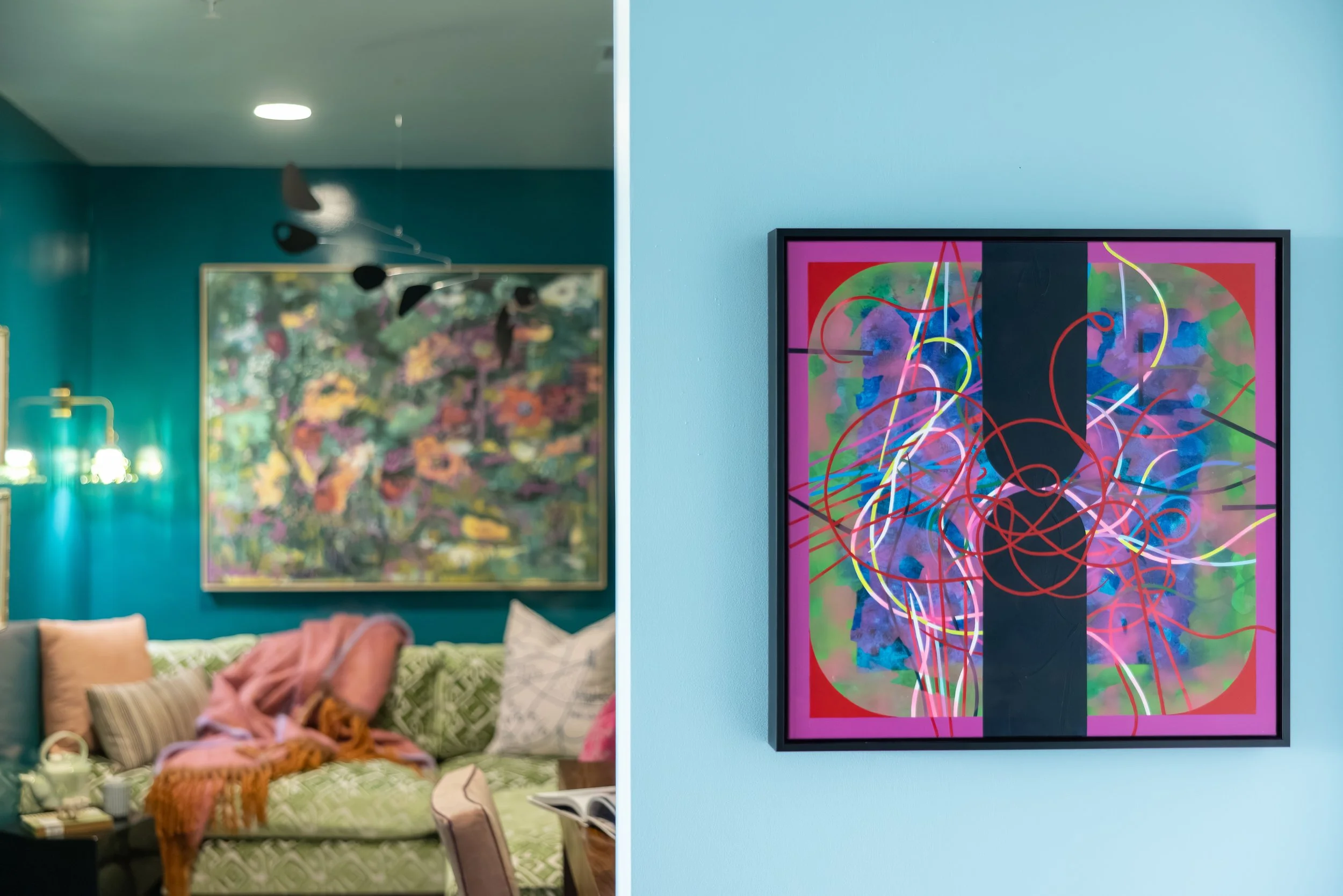 Side-by-side view of bedrooms in an art gallery, with colorful paintings on walls and varied furniture in both rooms.