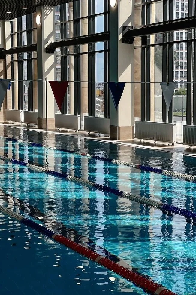 Indoor swimming pool with lane dividers, large windows, and triangular flags hanging from the ceiling.