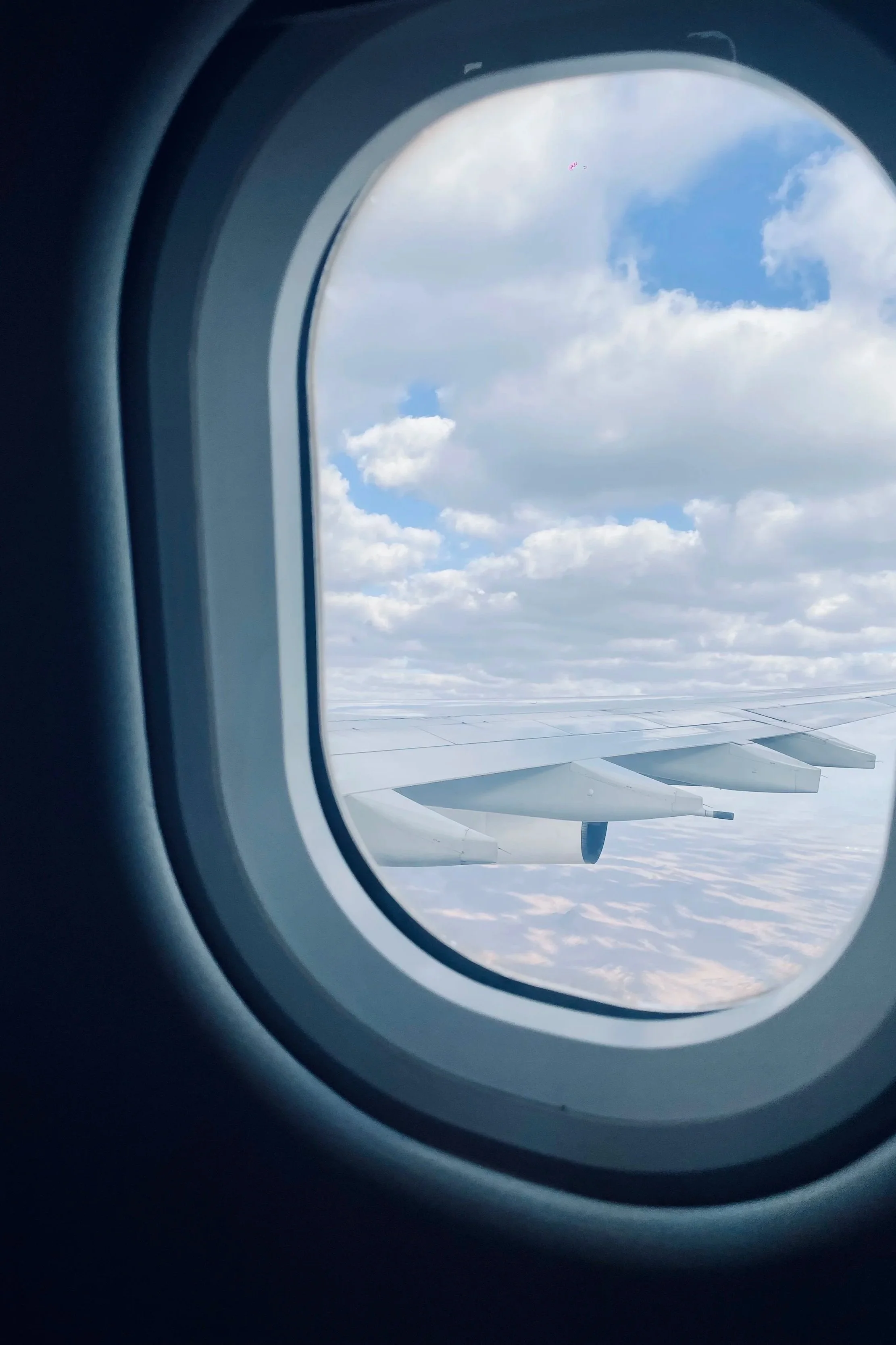 View of the sky and clouds through an airplane window with visible airplane wing.