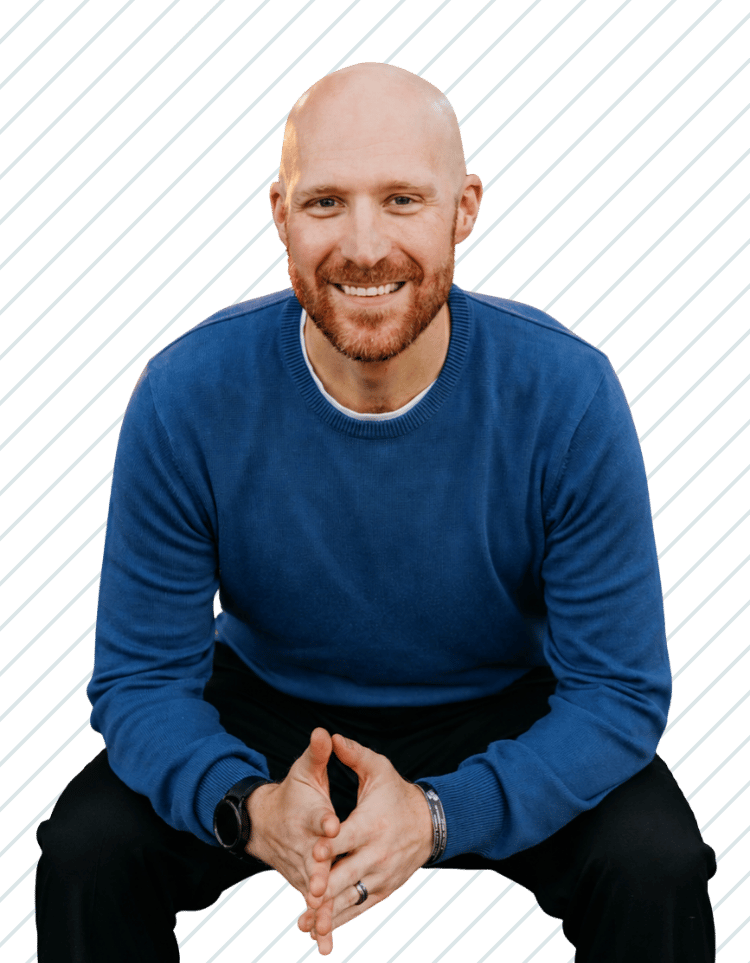 A smiling man with a beard and bald head wearing a blue sweater, sitting with hands clasped in front, Dr. Zachary Kuster of Bay Wellness Group.