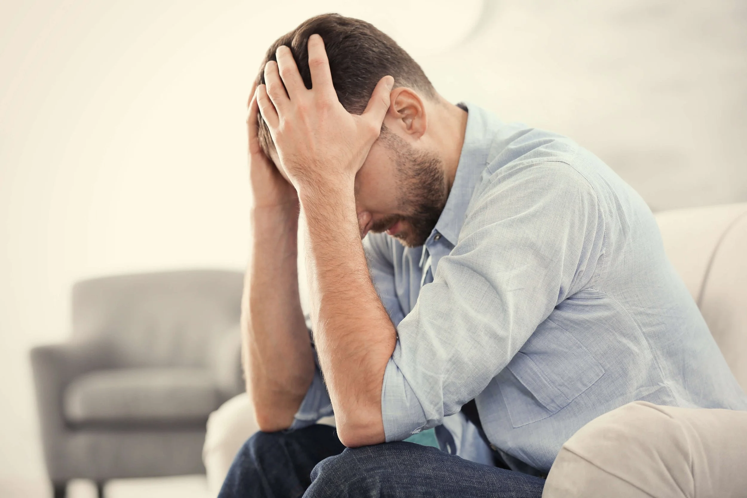 A man sitting with his hands holding his head, appearing distressed or upset.