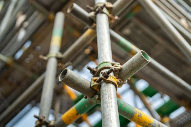 Close-up of metal scaffolding pipes connected with clamps, showing some green and yellow paint on the pipes.