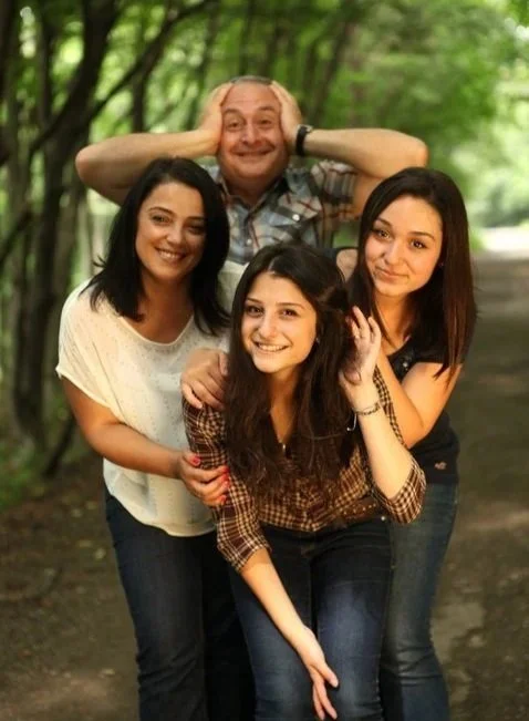 Group of four friends smiling and posing outdoors in a wooded area.