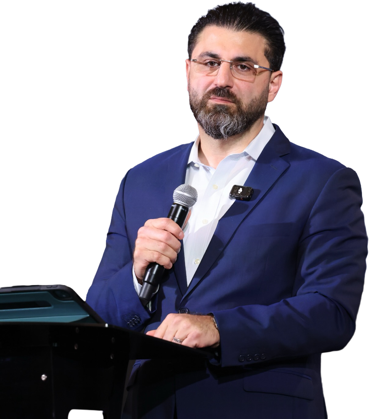 Մուգ մազերով, մորուքով և ակնոցներով տղամարդ՝ հագած մուգ կապույտ բաճկոն և սպիտակ վերնաշապիկ, միկրոֆոնը ձեռքին և կանգնած է ամբիոնի մոտ։