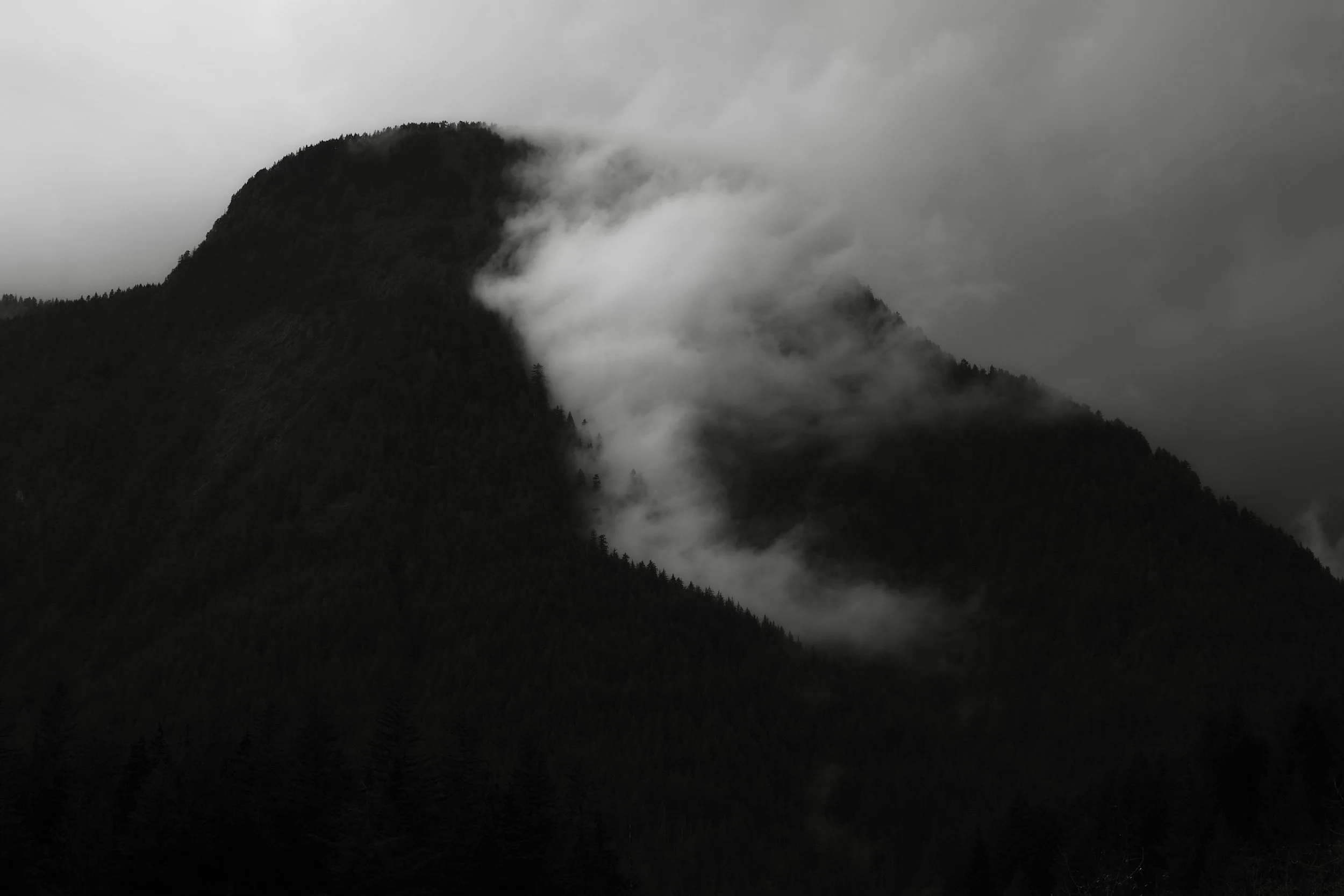 A black and white photo of a mountain shrouded in fog and low clouds.