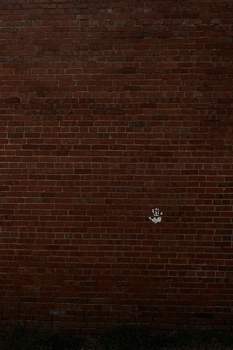 A white handprint spray-painted on a red brick wall.