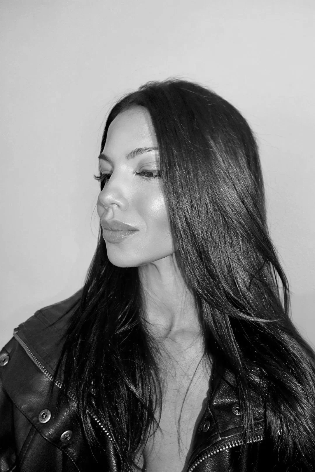 Angela Forte with long, dark hair and a slight smile, wearing a leather jacket, facing slightly to the left against a plain background.