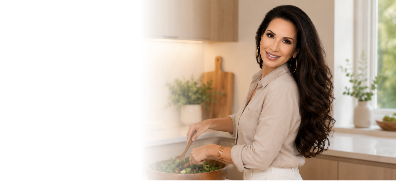Woman with long dark hair smiling while preparing a salad in a bright, modern kitchen.