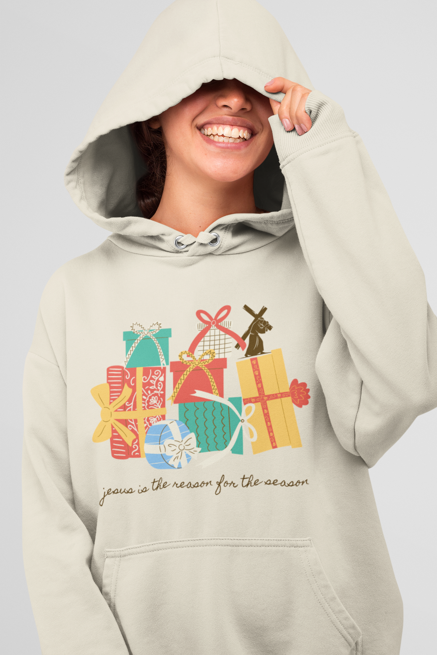 A person wearing a light-colored hoodie with a Christmas-themed design and the phrase "Jesus is the reason for the season," smiling with their face partially obscured by the hood.