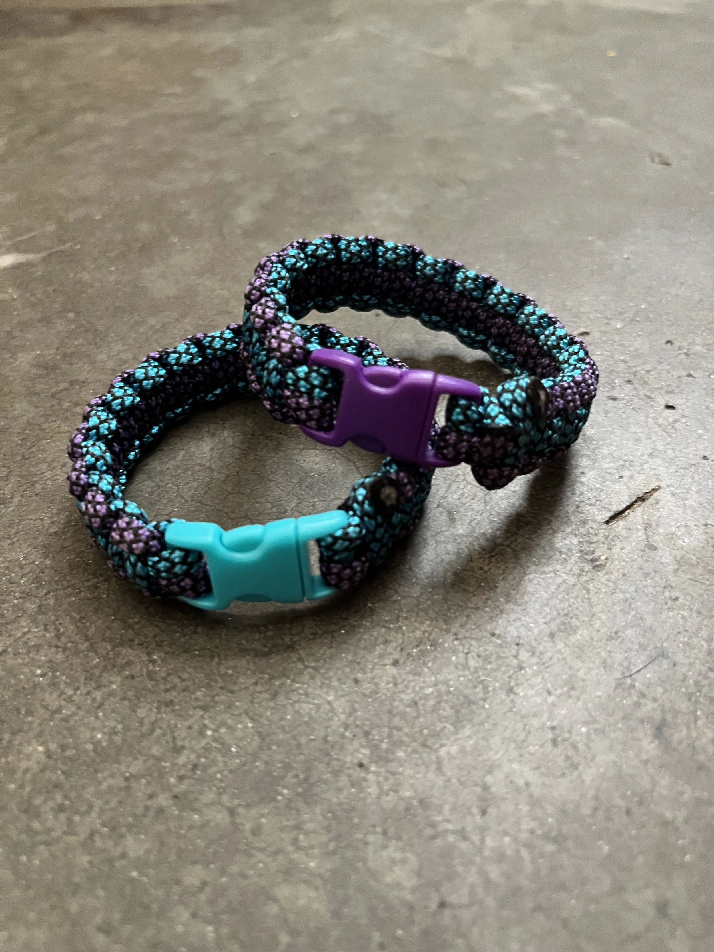 A colorful braided bracelet with a purple clasp on a textured surface.