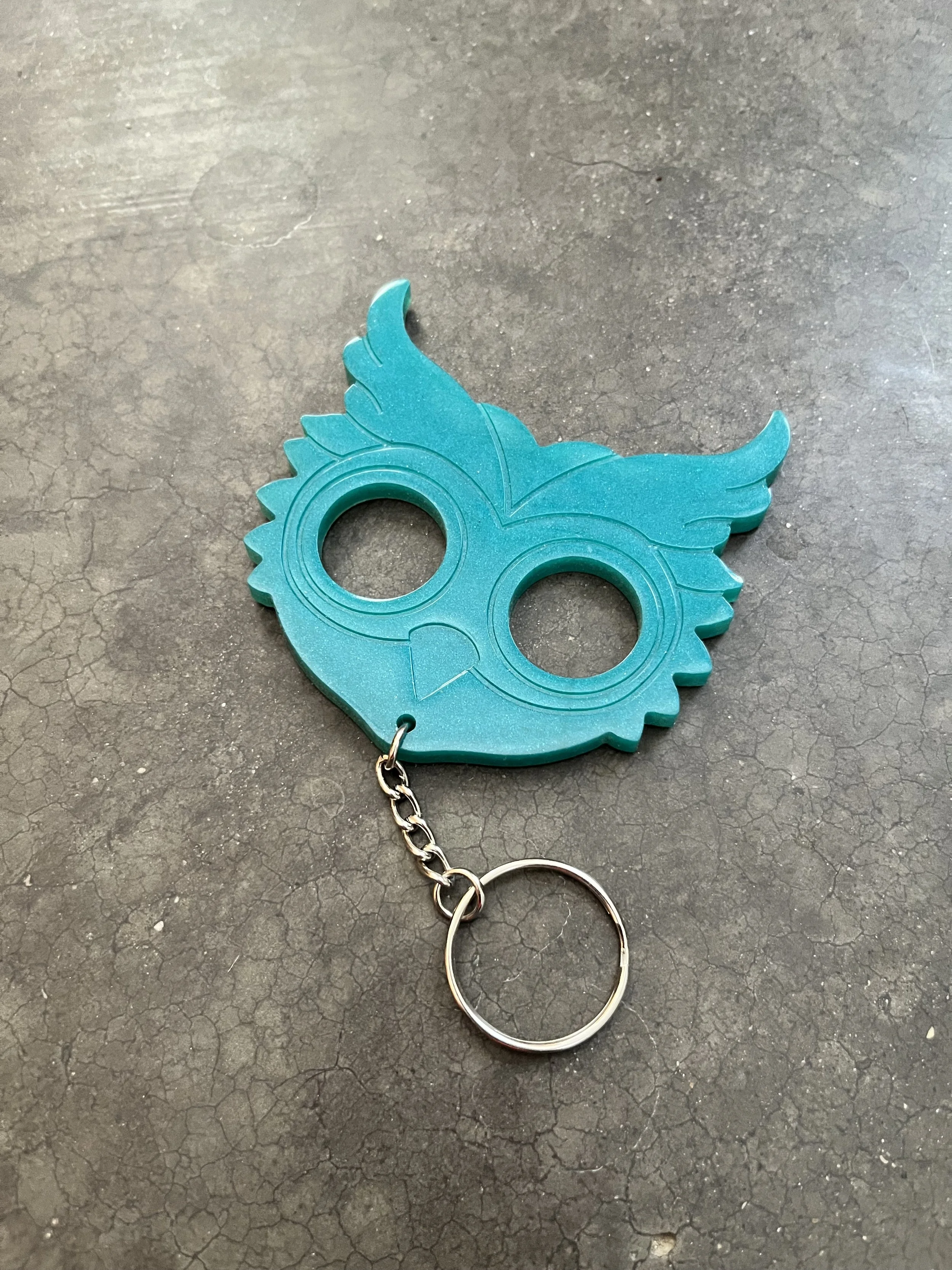A teal-colored emergency keychain, placed on a dark textured surface.