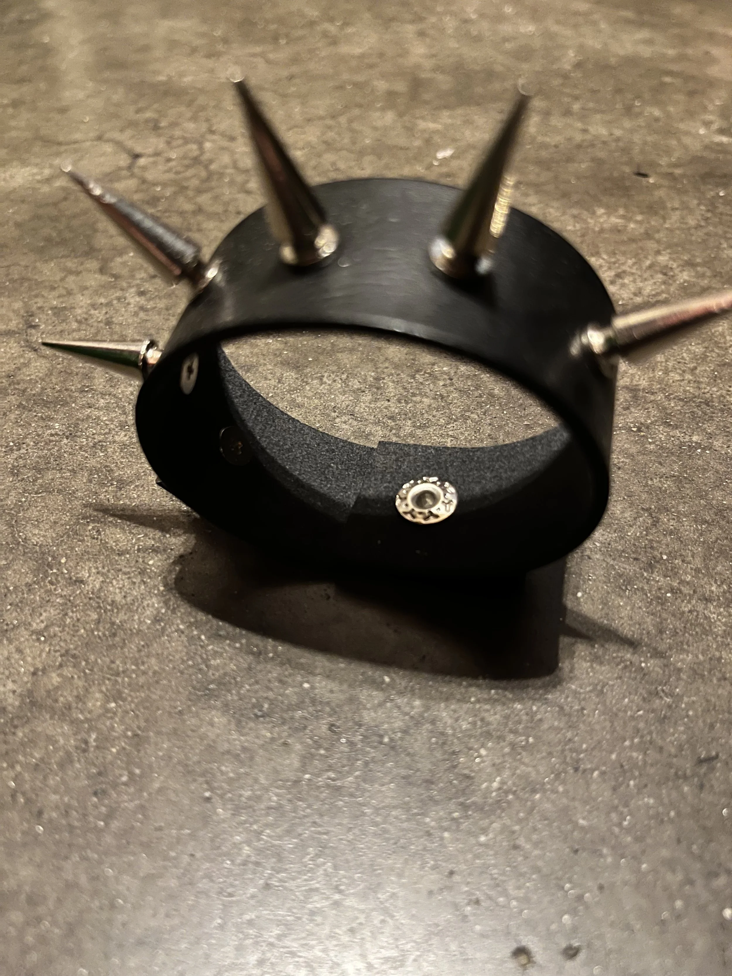 A black leather wristband with three silver spikes attached, placed on a gray textured surface.
