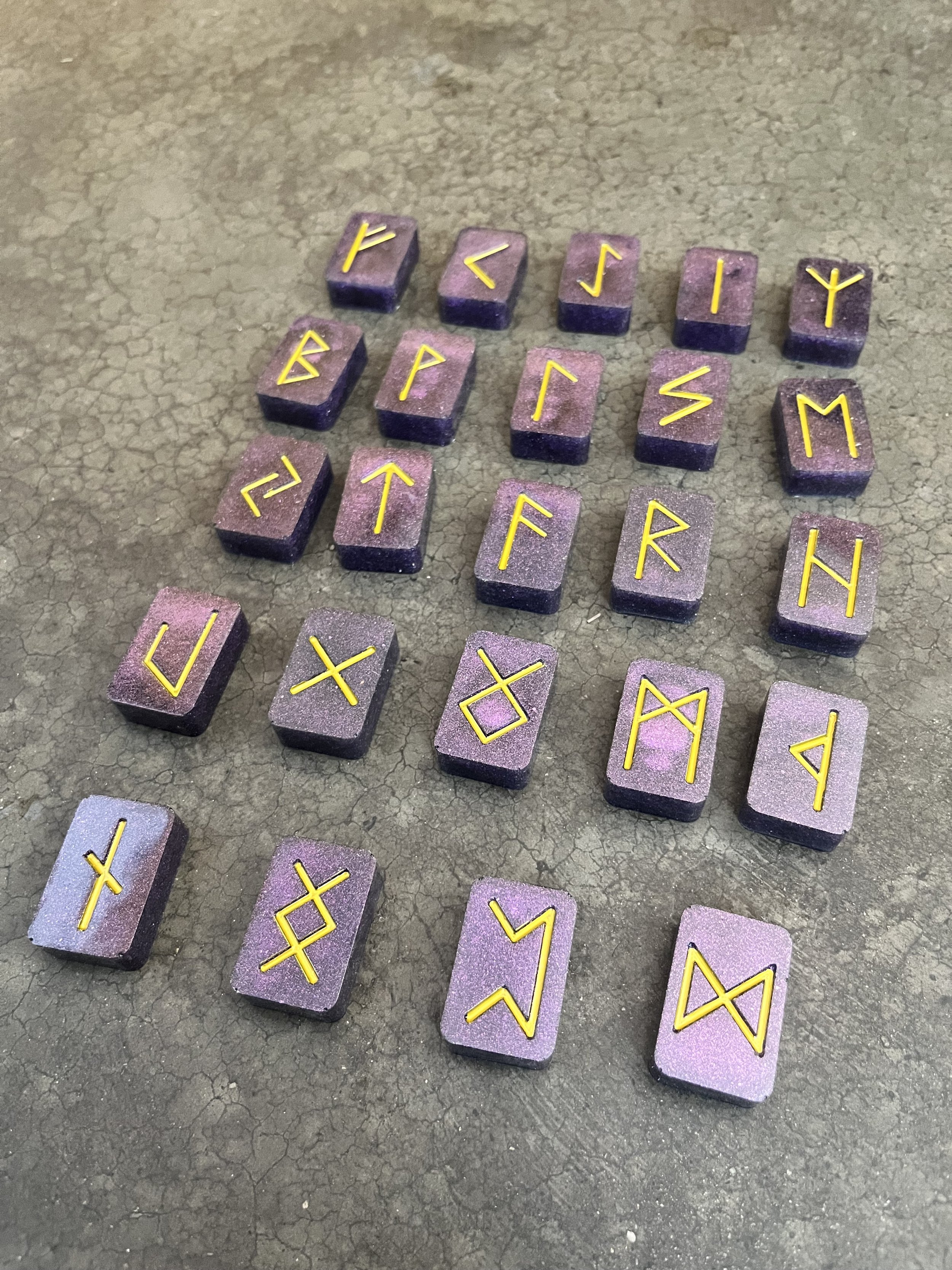 A collection of purple rune stones made from epoxy resin scattered on a cracked concrete surface.