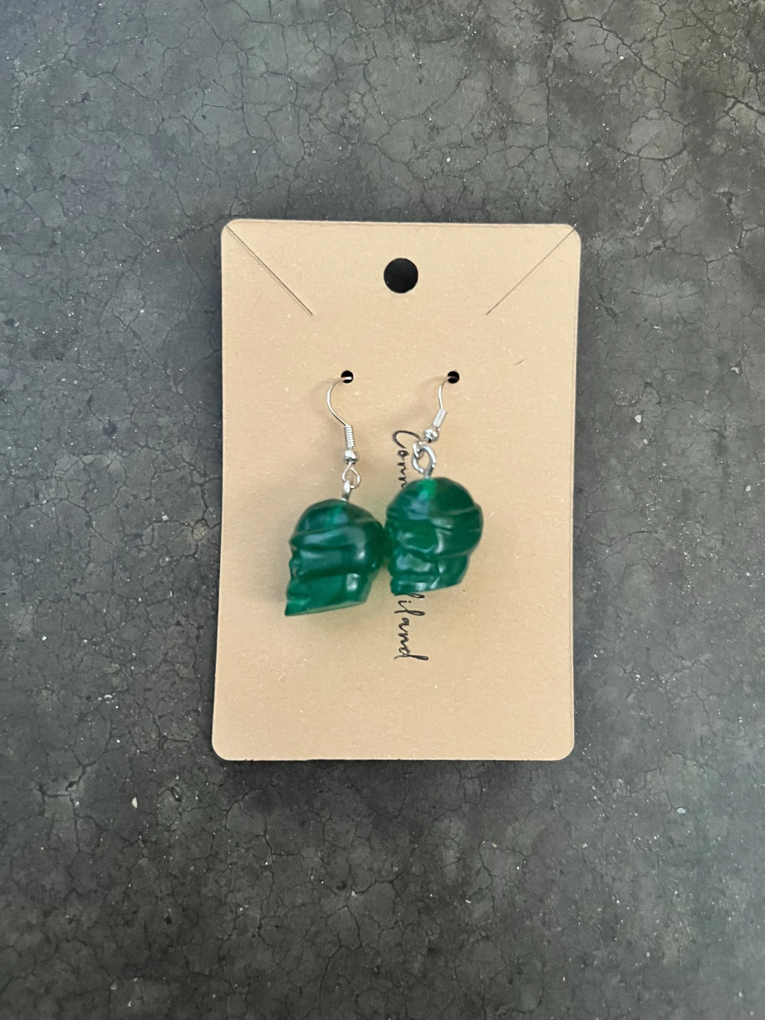 A pair of epoxy resin earrings on a beige cardboard display card placed on a cracked black surface.