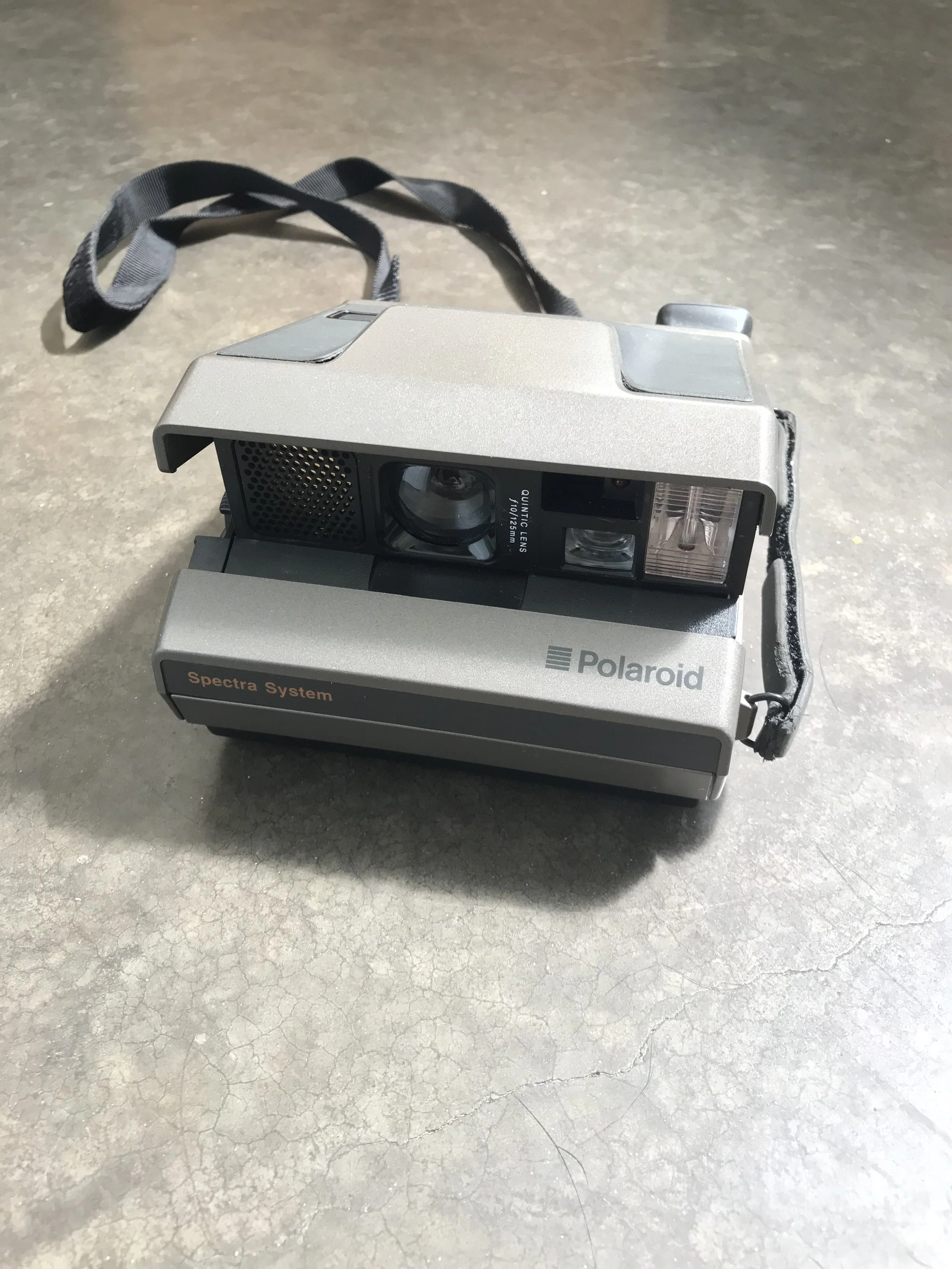 A vintage Polaroid Spectra System instant film camera resting on a cracked concrete floor.