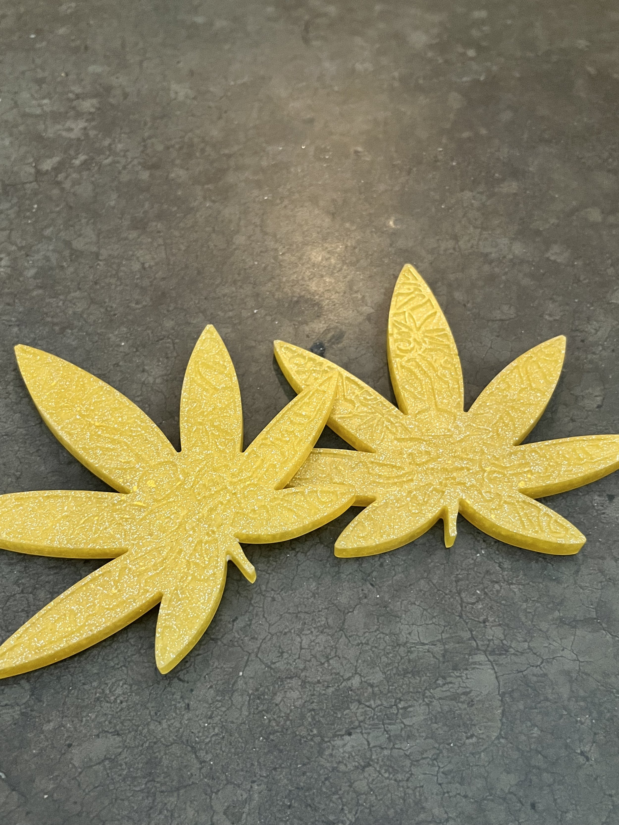 Close-up of yellow wax cutout shaped like leaves on a dark textured surface.