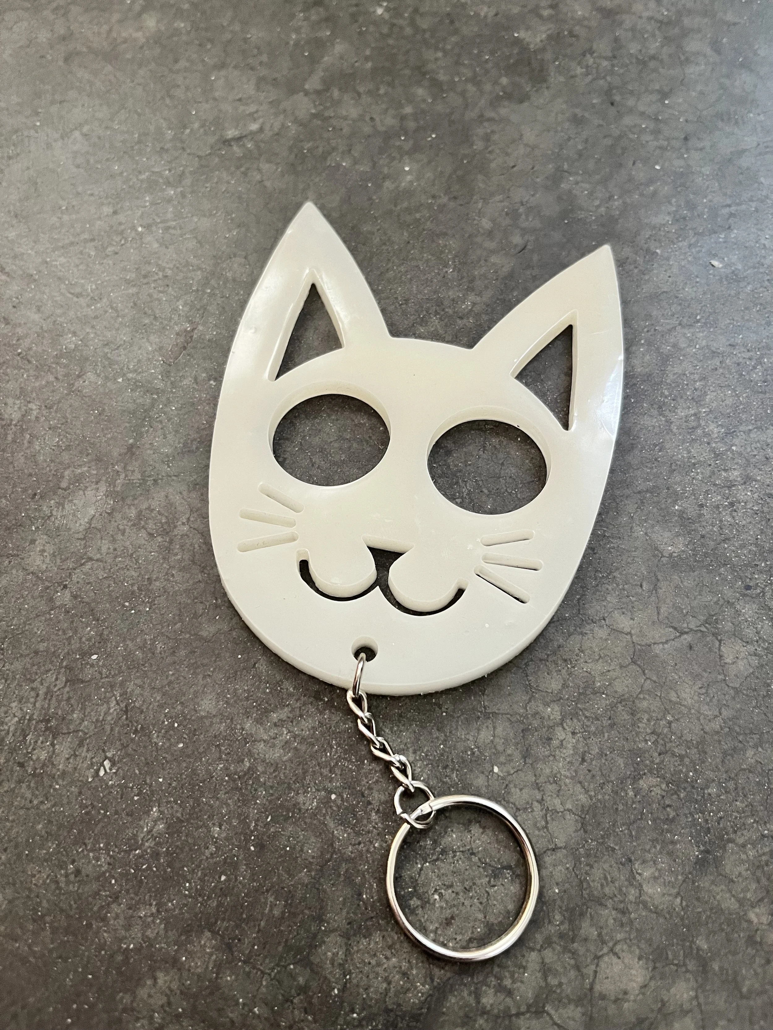 A stylized emergency keychain shaped like a cat's face, lying on a dark, textured surface.