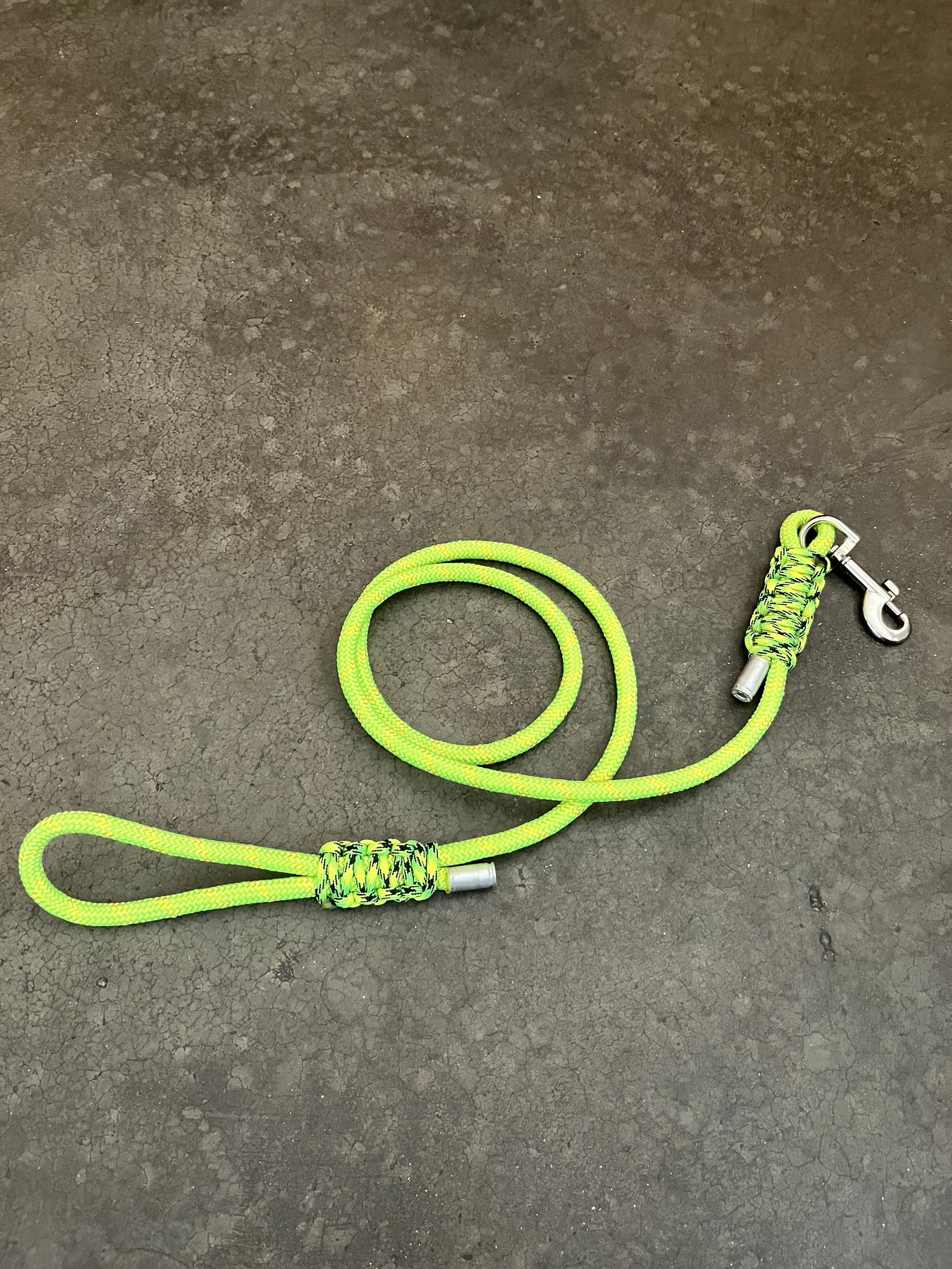A neon green rope with a metal clip at one end lies on a cracked dark asphalt surface.