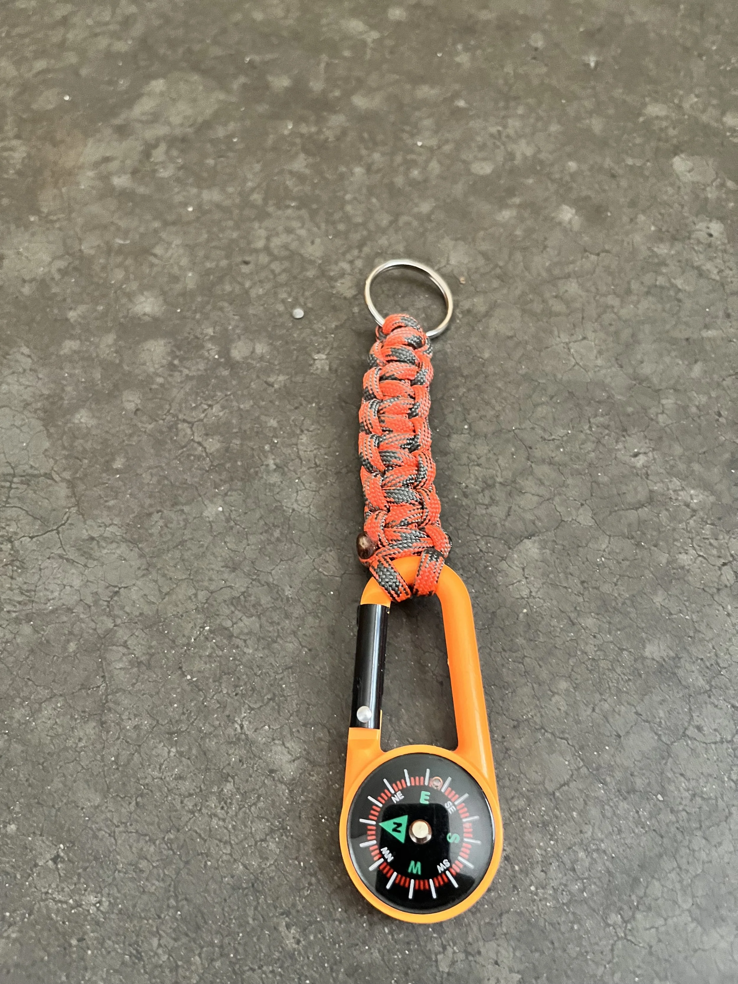 A handmade orange paracord keychain with a compass attached.