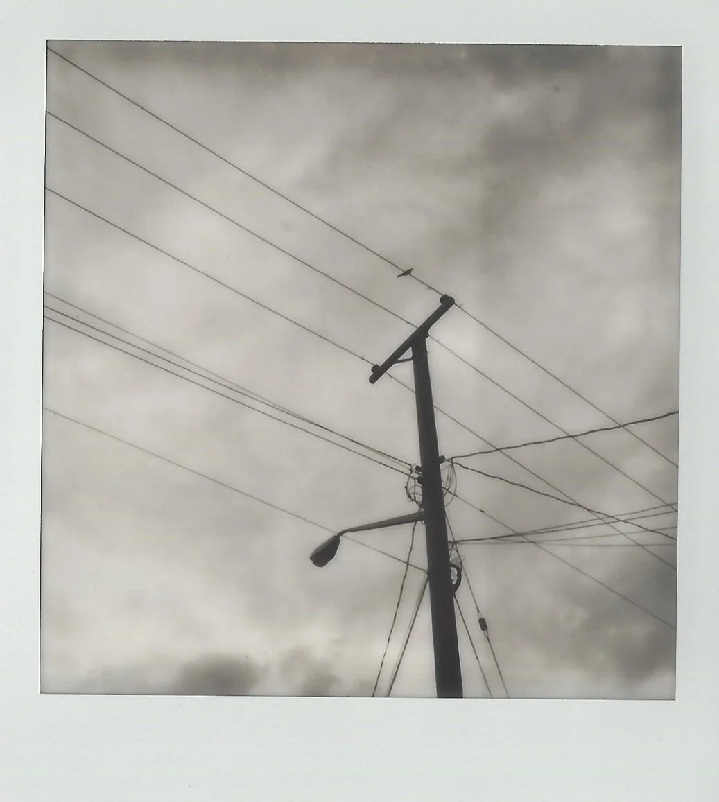 A utility pole with power lines and a street light against a cloudy sky.