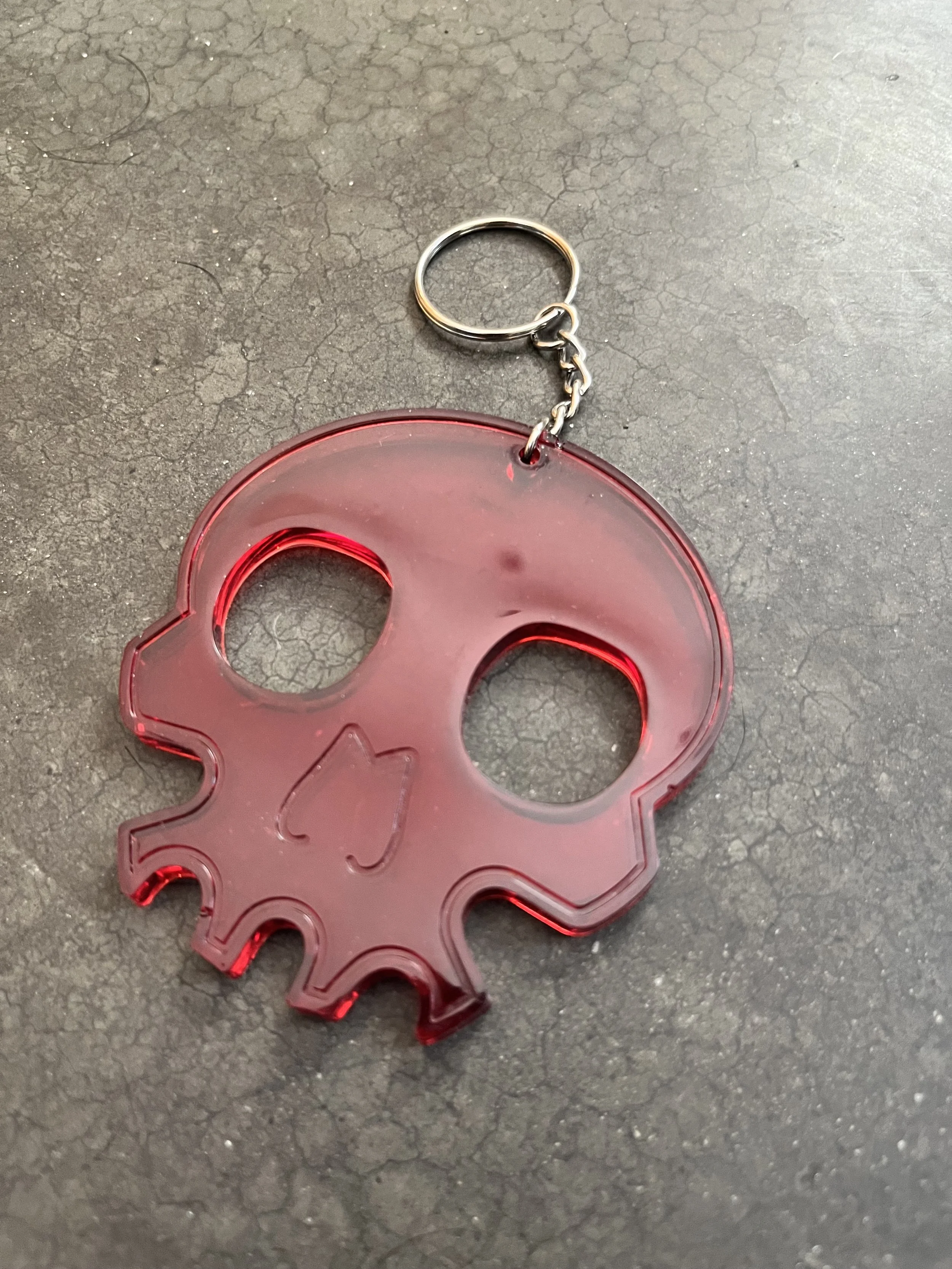 A handmade epoxy resin red skull-shaped keychain, resting on a dark, textured surface.