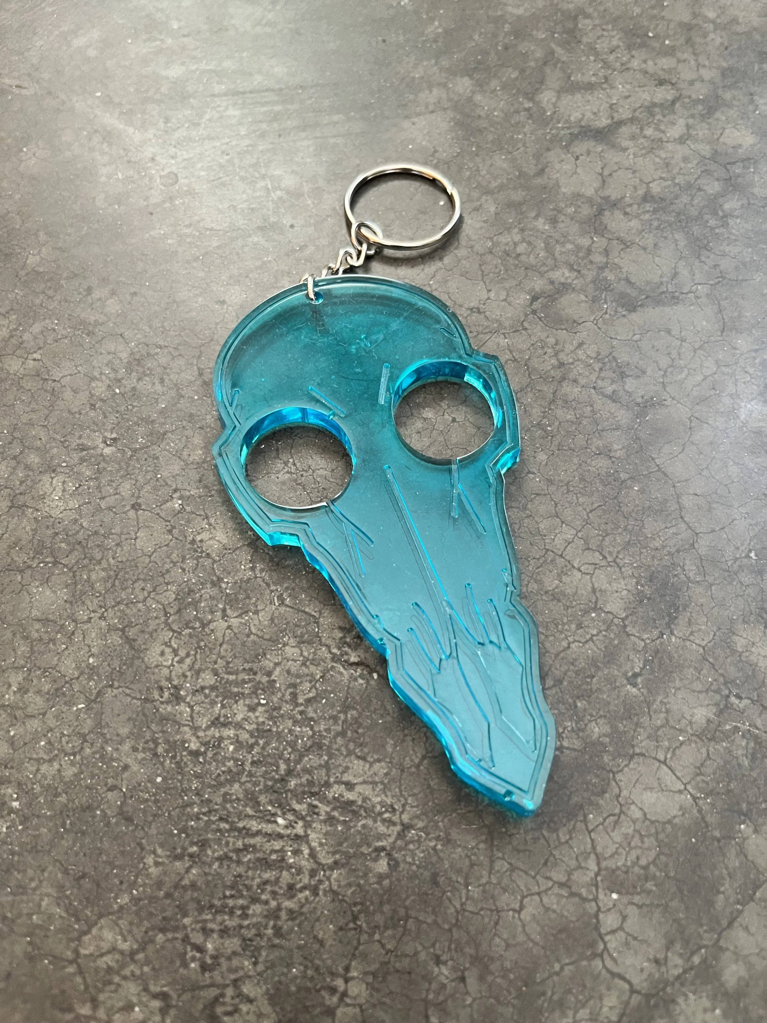 A blue translucent resin epoxy emergency keychain, lying on a rough, cracked black surface.