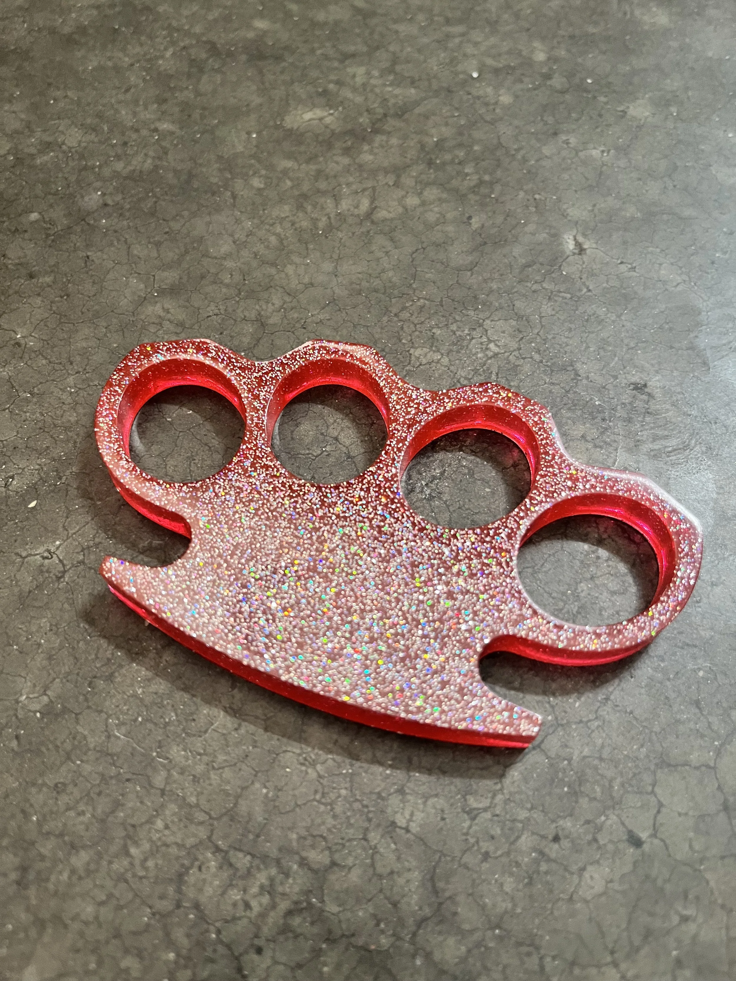 Red glittery epoxy resin knuckle keychain on a cracked asphalt surface.
