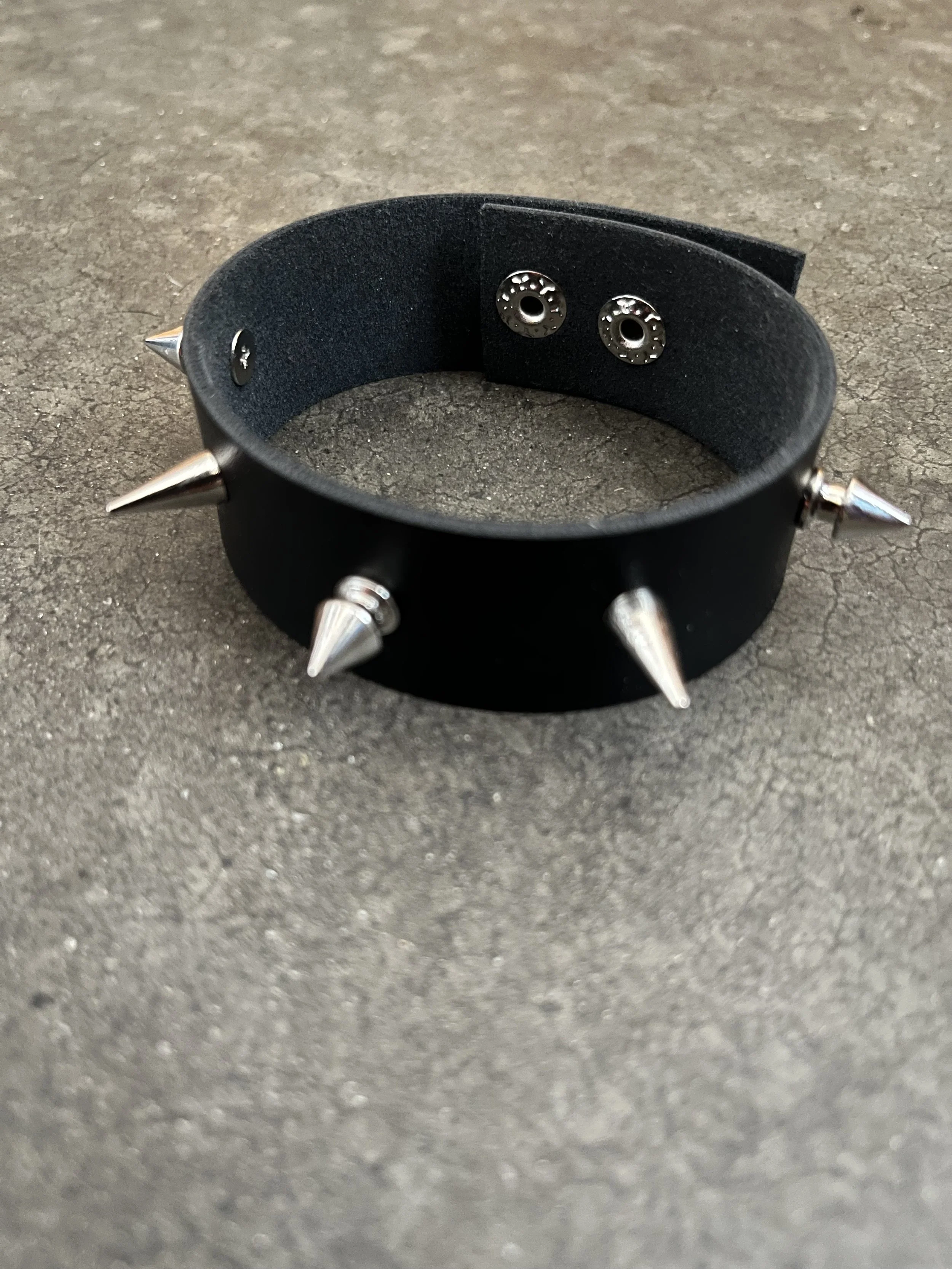 A black leather choker with metal spikes and silver studs on a dark textured surface.