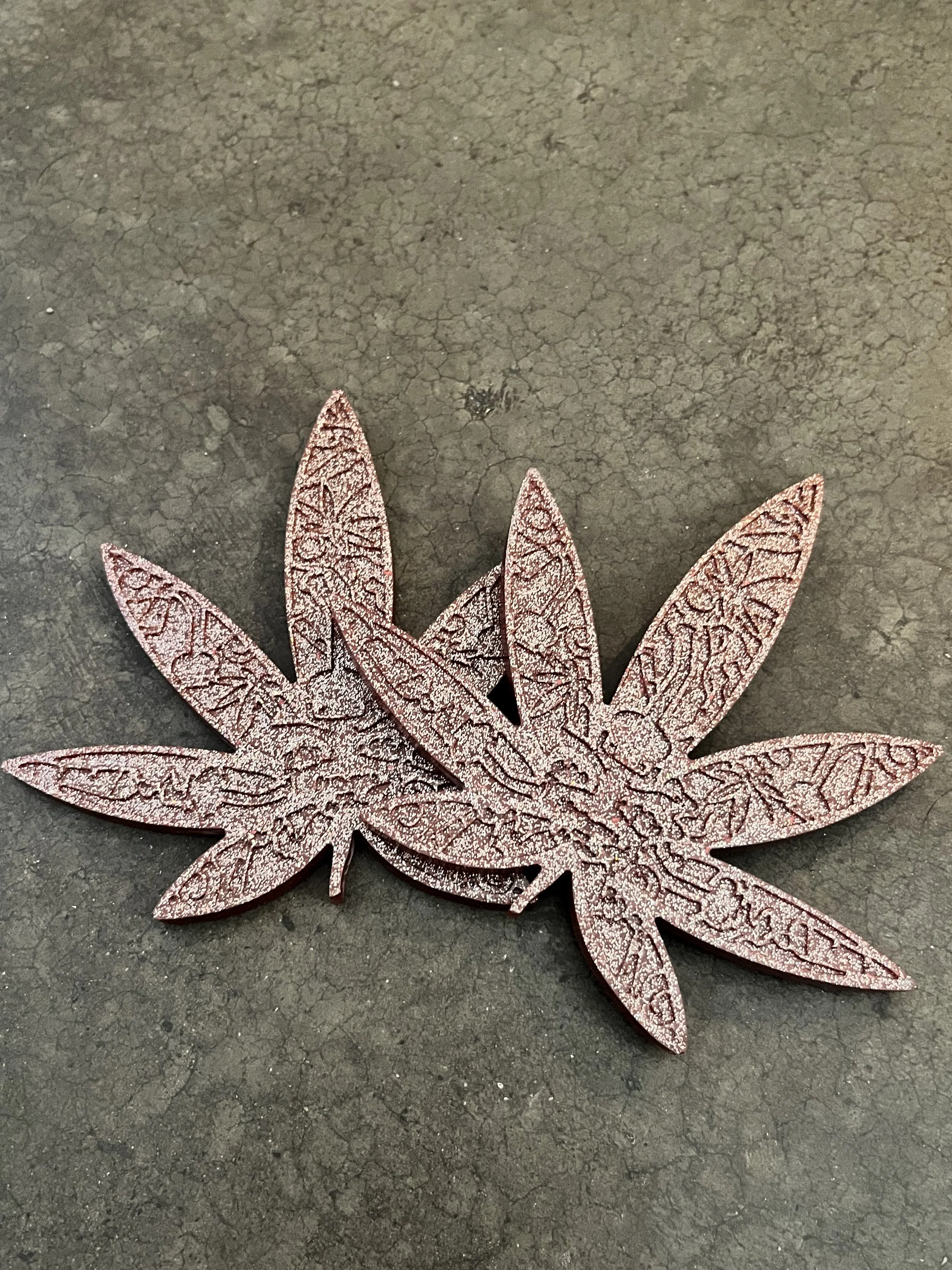 Pink decorative leaf-shaped cutouts with intricate patterns placed on a dark, cracked surface.