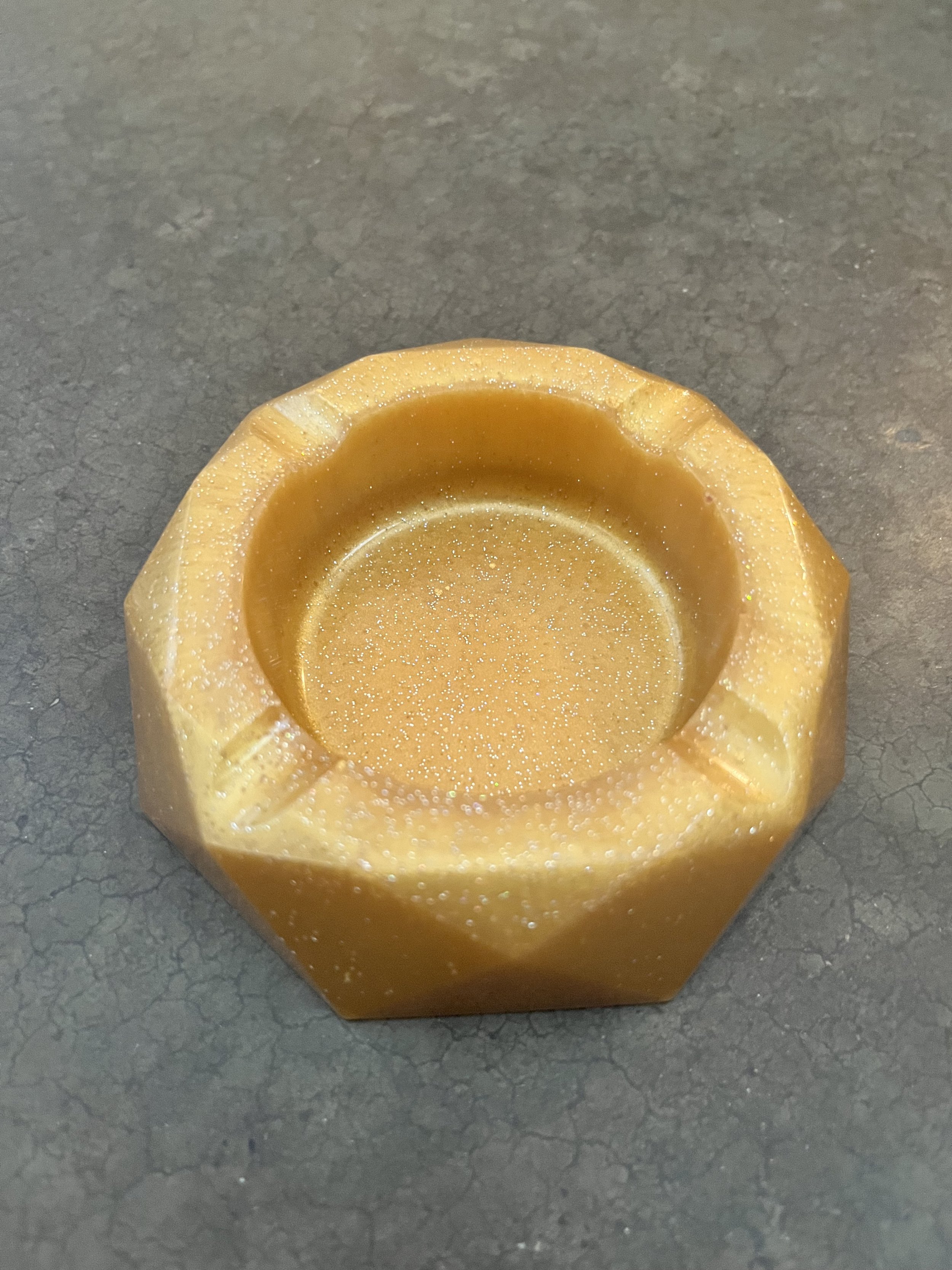 Close-up of a yellow ash tray with a textured surface, set on a dark gray, cracked surface.