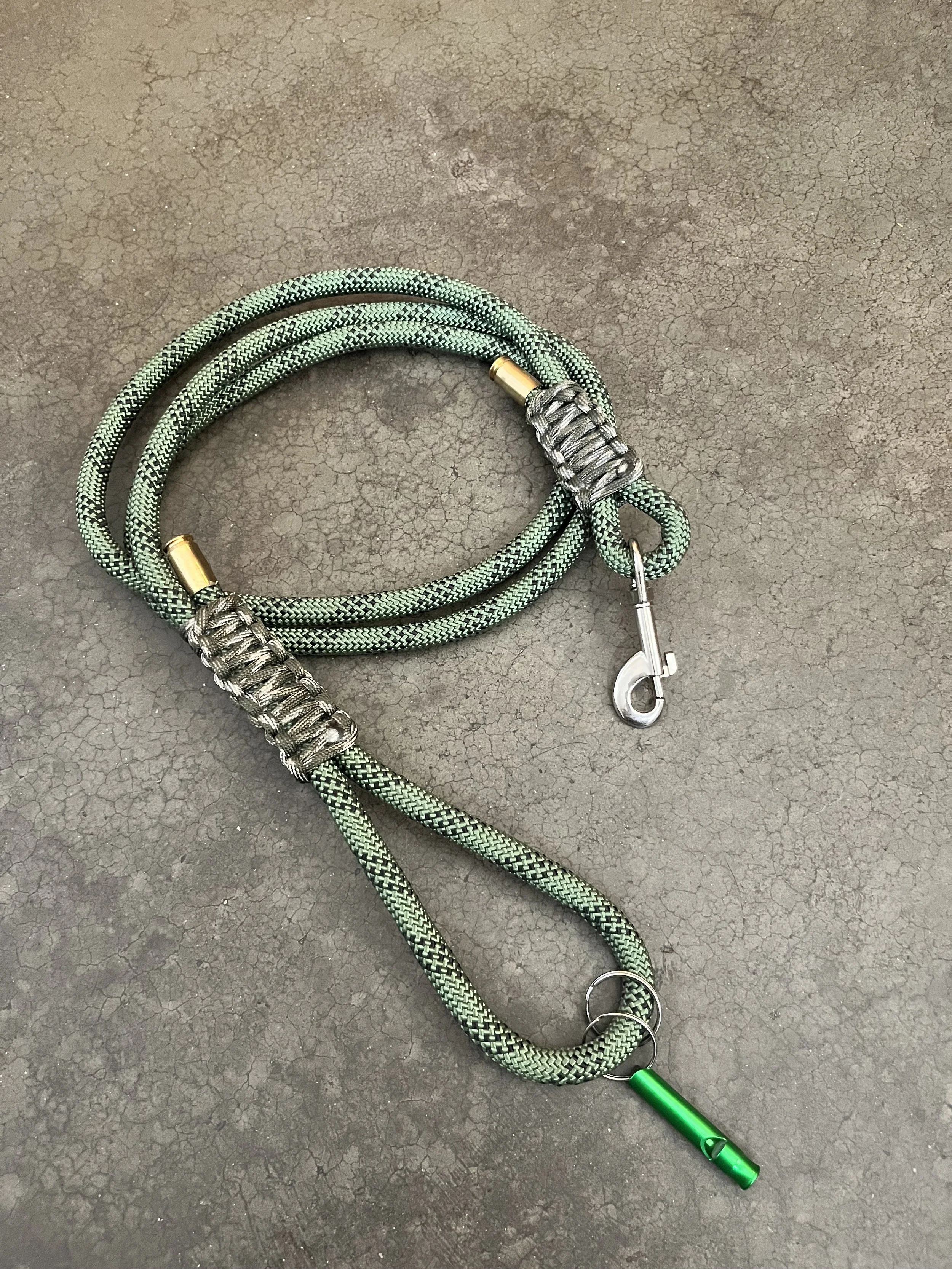 A handmade green and black braided dog leash with a whistle.