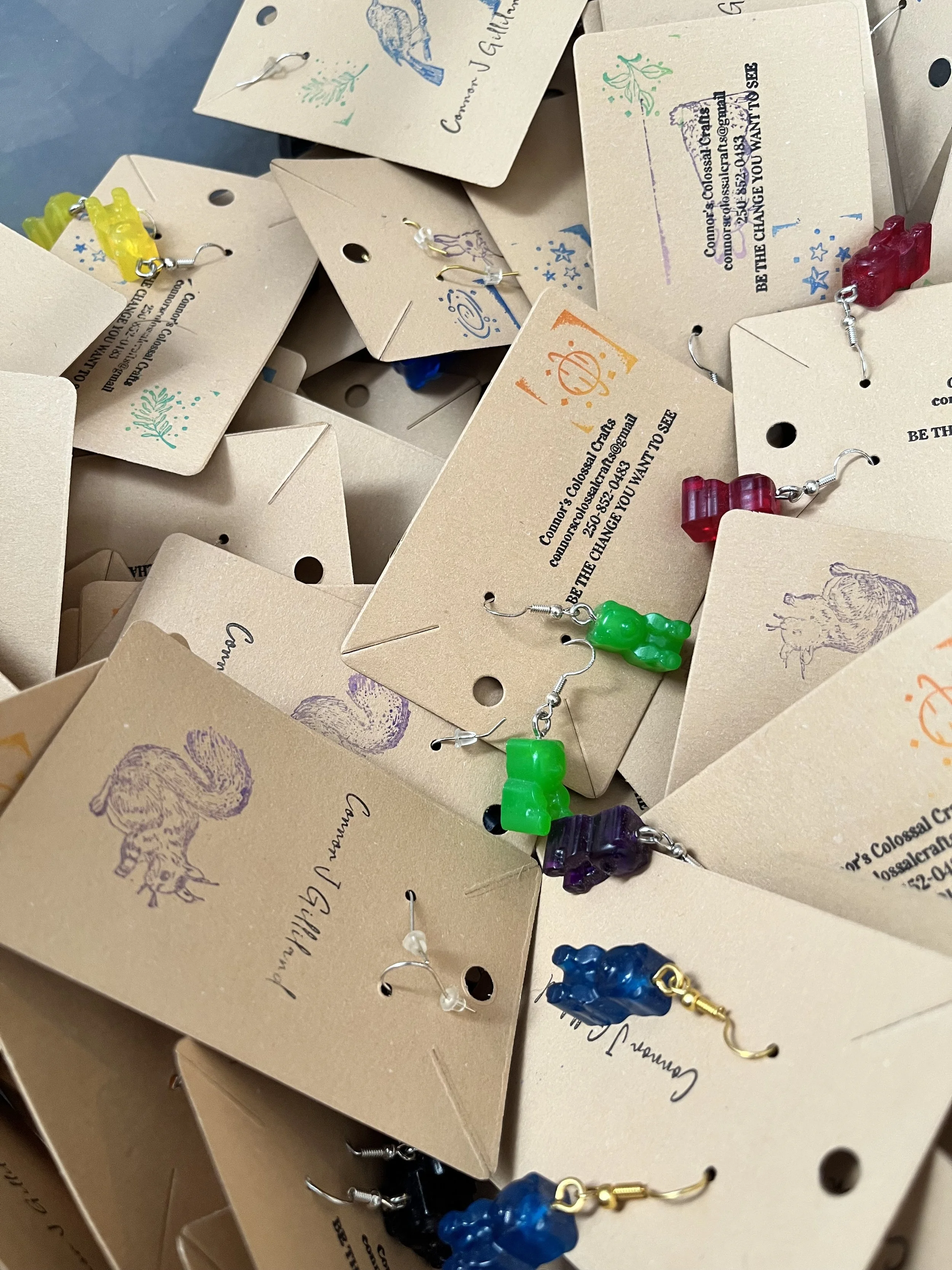 Multiple pairs of colorful gummy bear earrings hanging on display cards with text and designs.