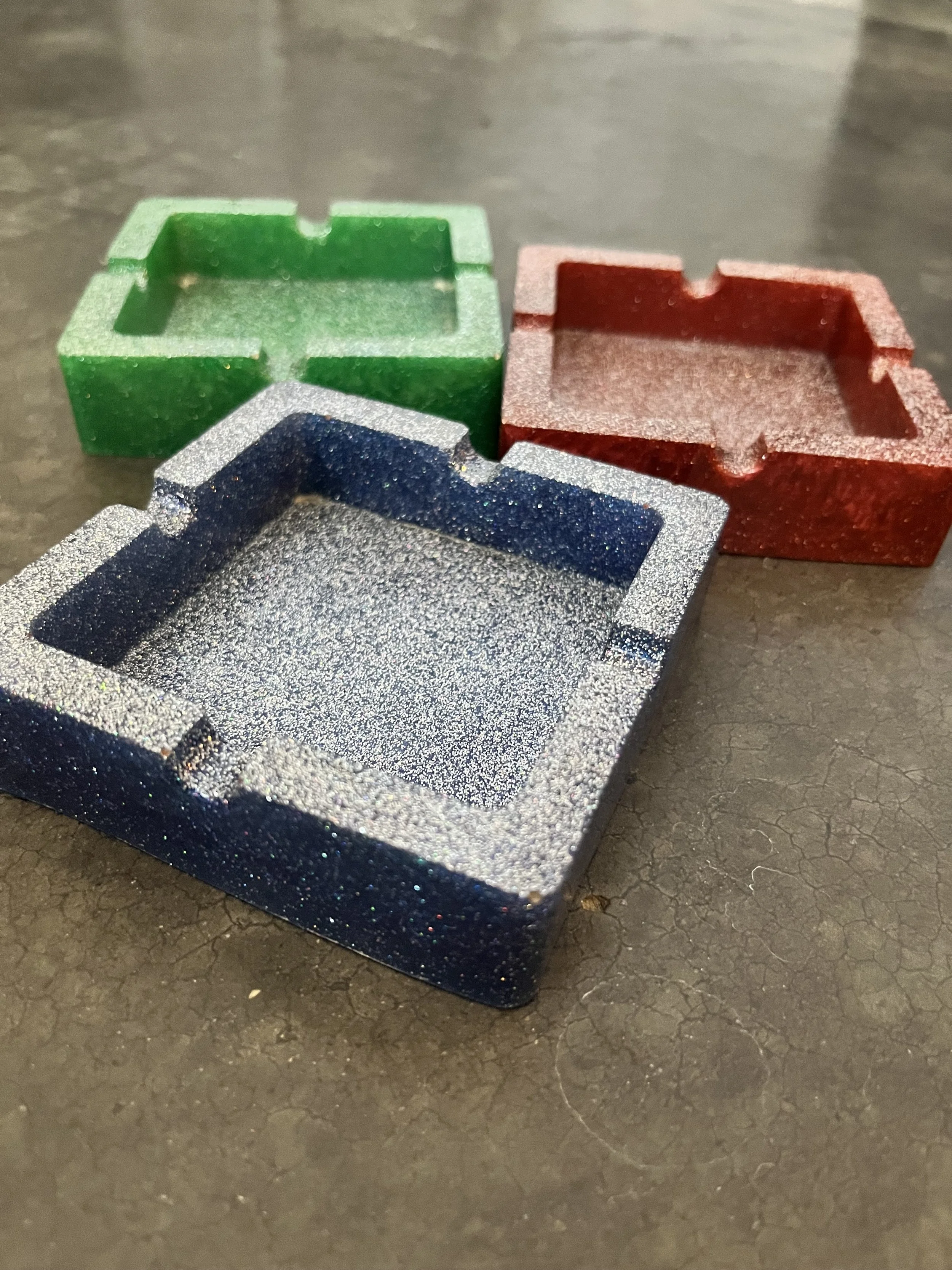 Close-up of three colorful ash trays placed on a textured dark surface.