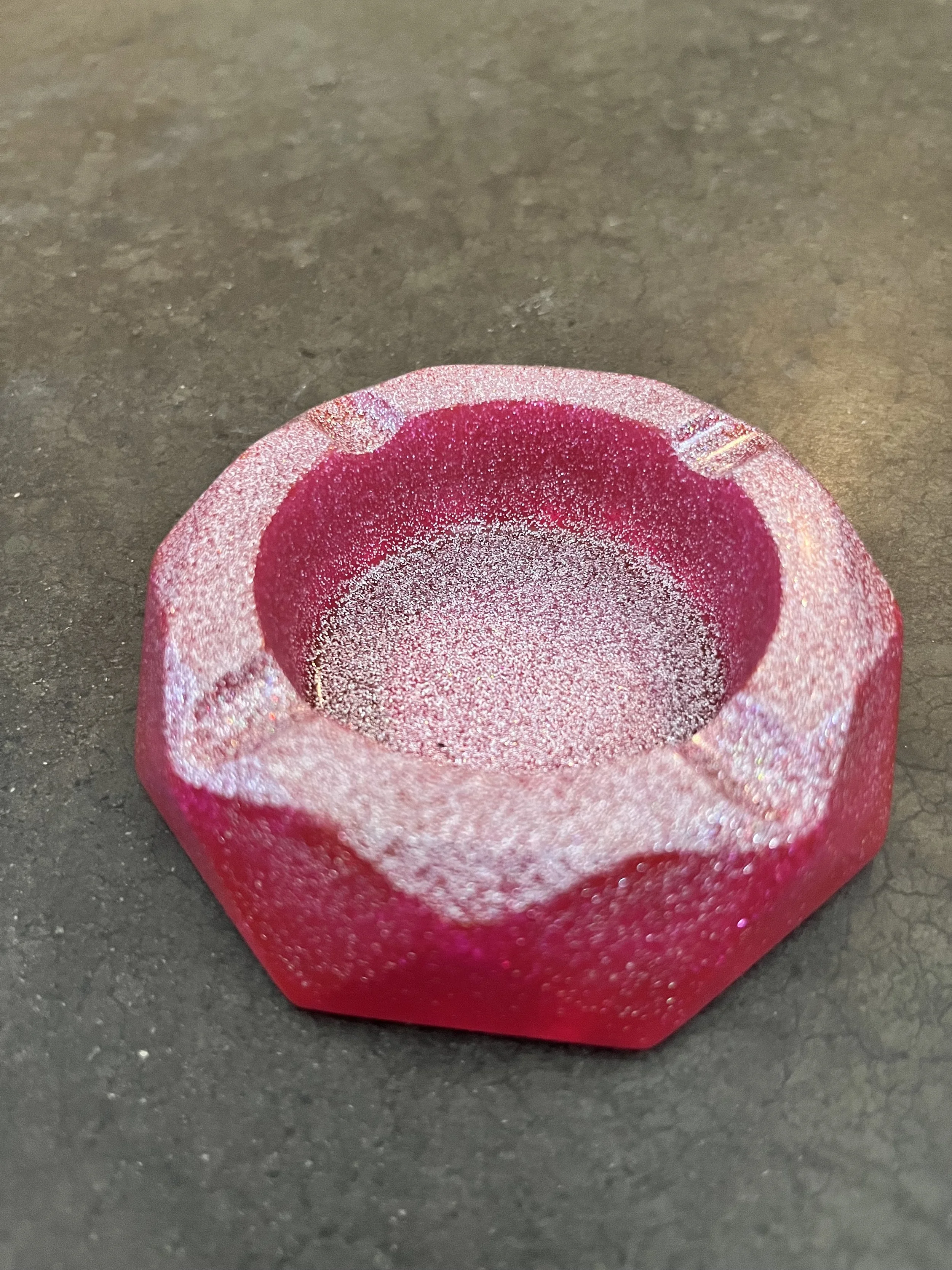 Close-up of a small, pink, sparkly candle holder with a glittery finish on a dark surface.