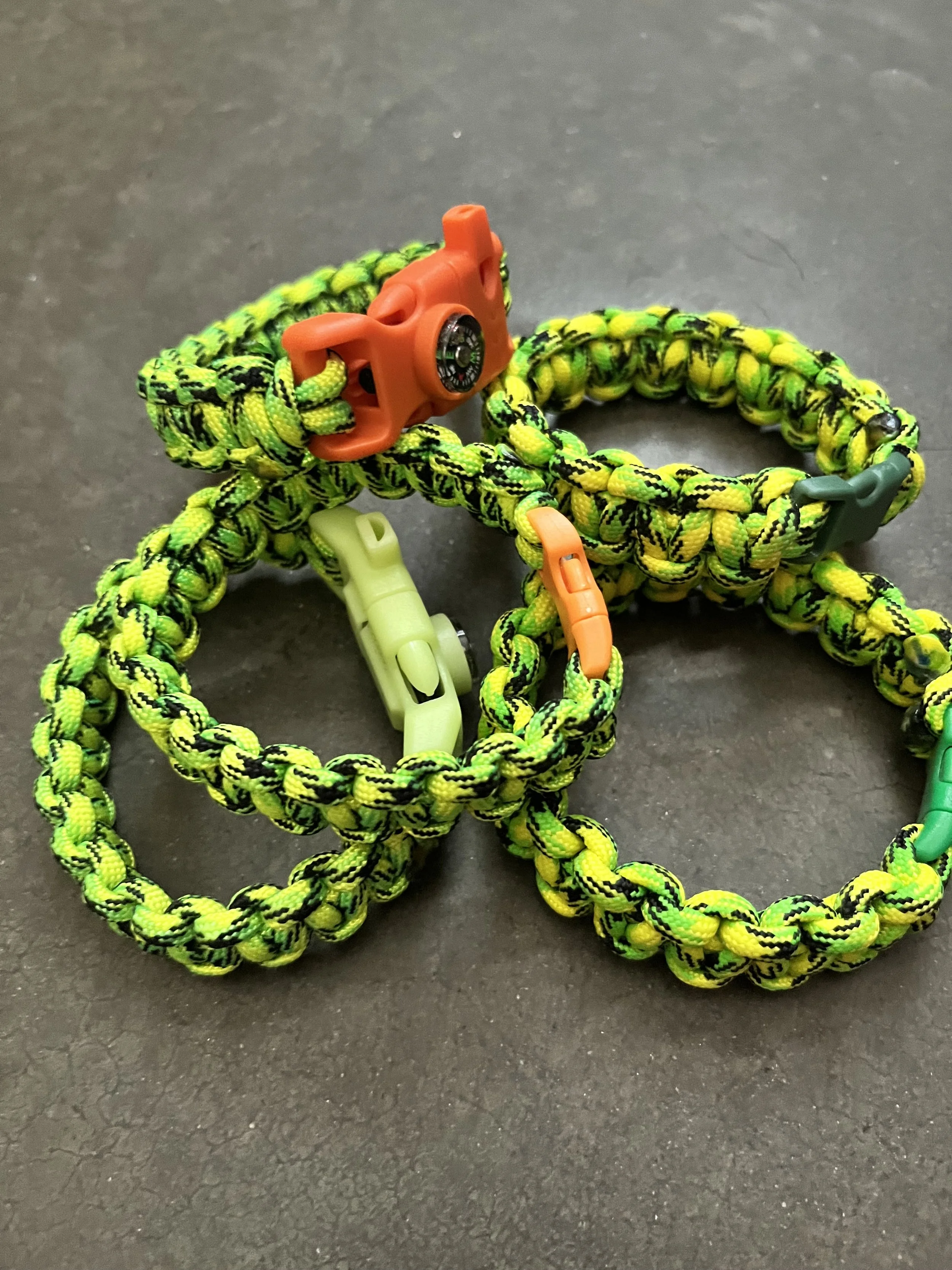 Several handmade neon green paracord bracelets with whistles and compasses.