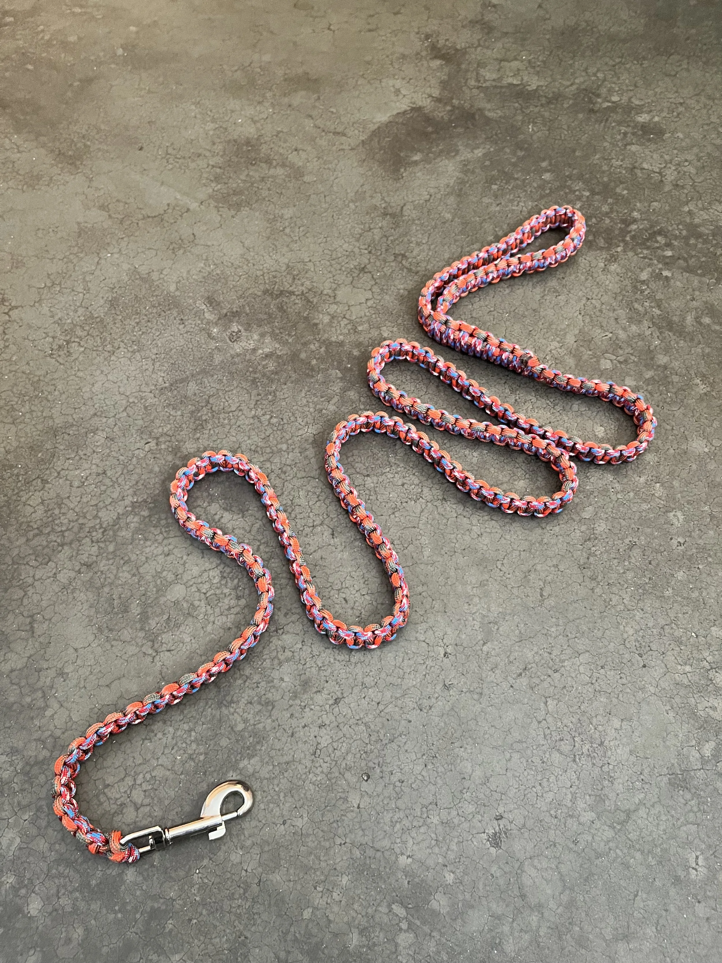 A colorful braided dog leash with a metal clasp lying on a cracked gray concrete surface.