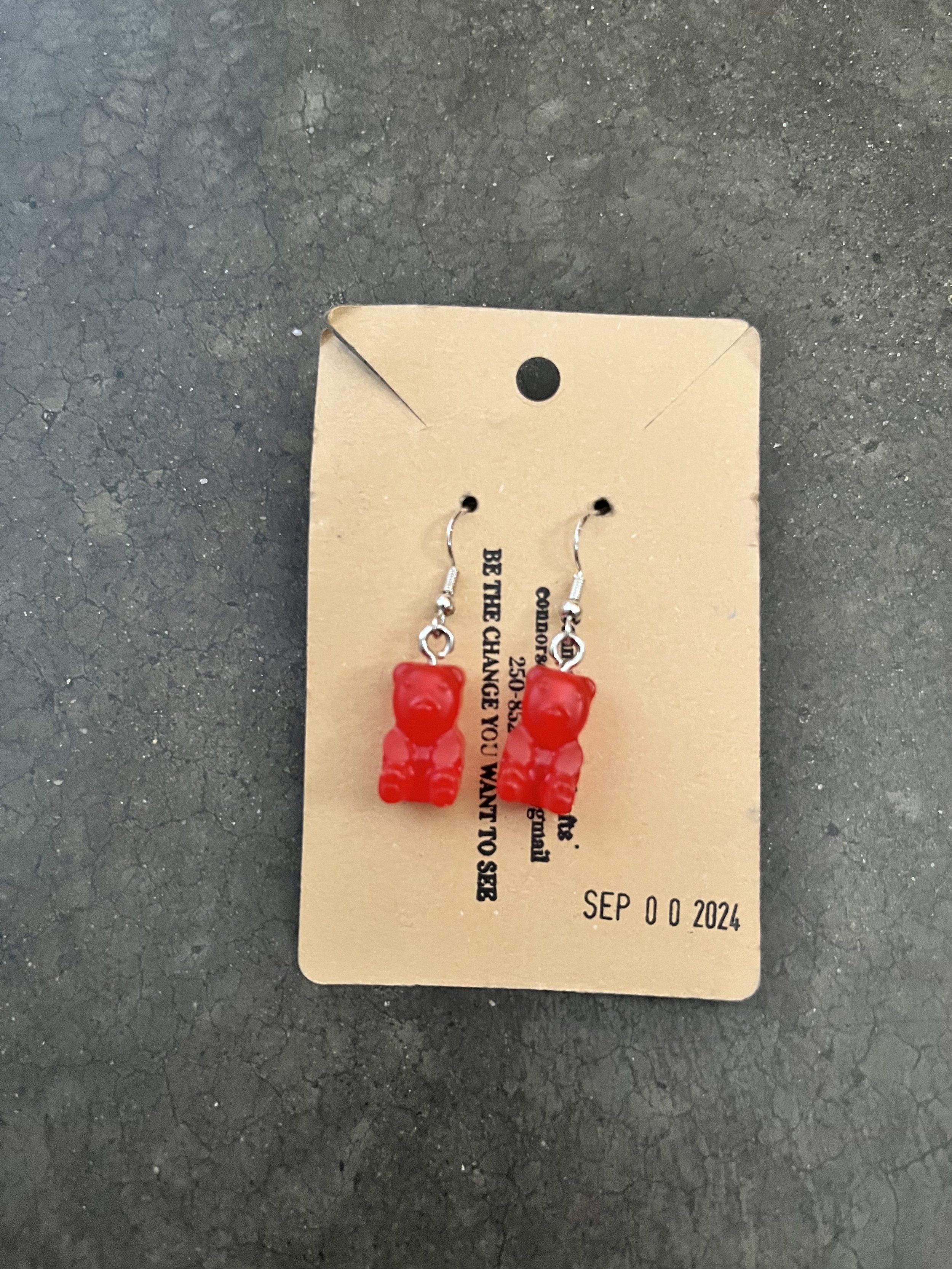 A handmade pair of red gummy bear earrings on a beige jewelry card.