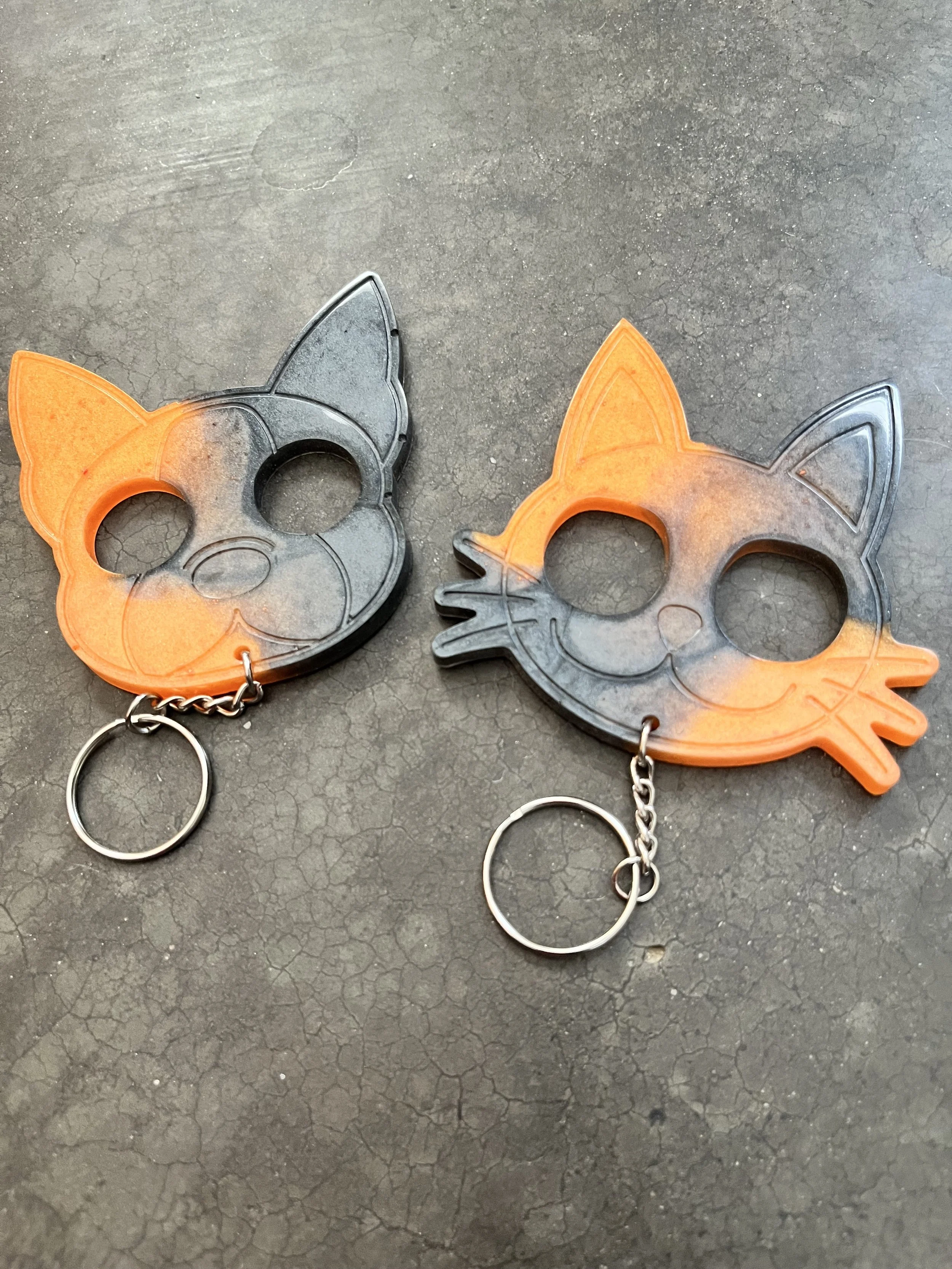Two resin epoxy emergency keychains,black and orange, on a cracked surface.
