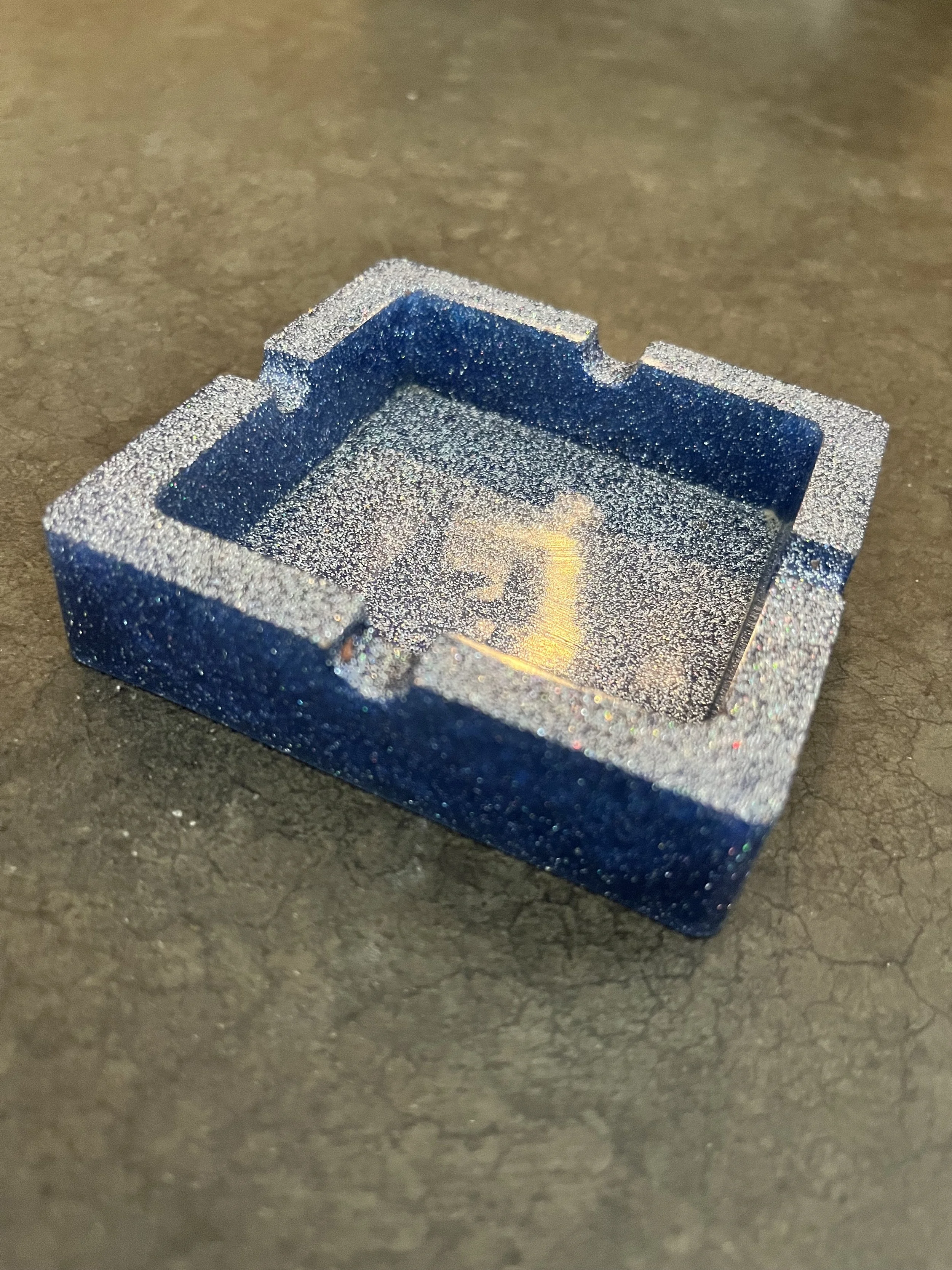Close-up of a metallic blue and silver glittery ash tray on a dark surface.