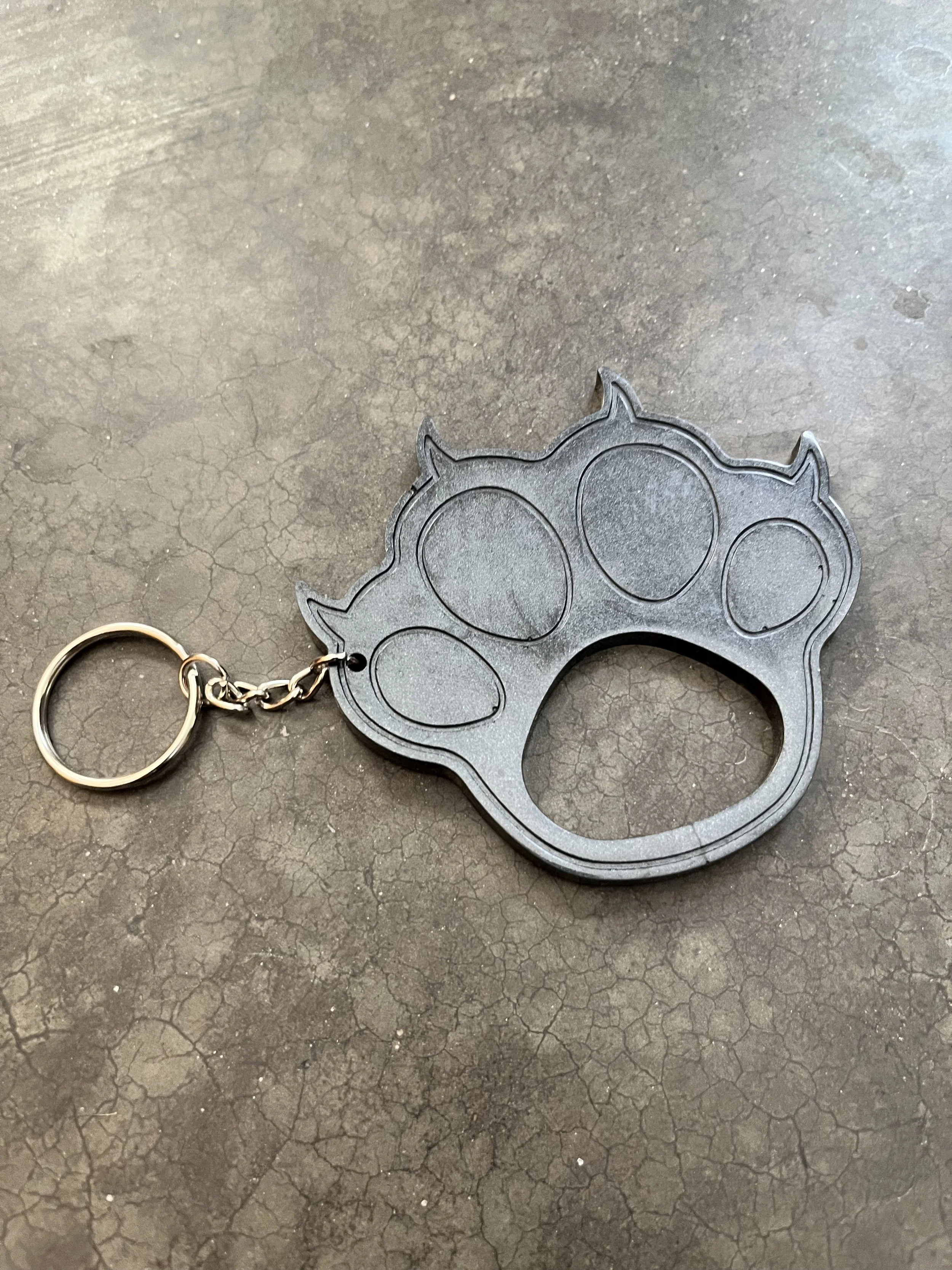 A black cat-paw haped knuckles keychain on a textured, cracked dark gray surface.