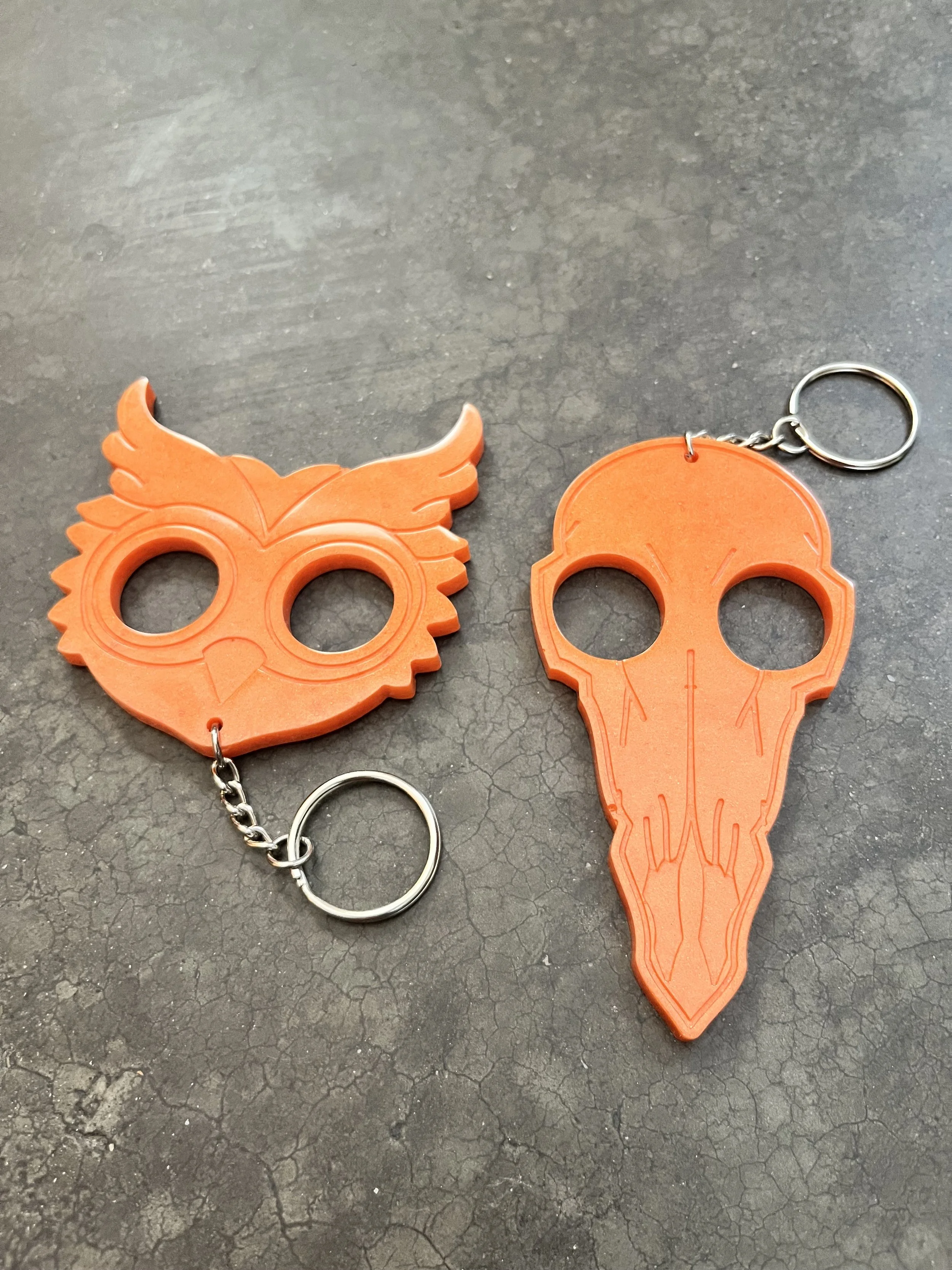 Two orange keychains with spooky designs on a dark, cracked surface.