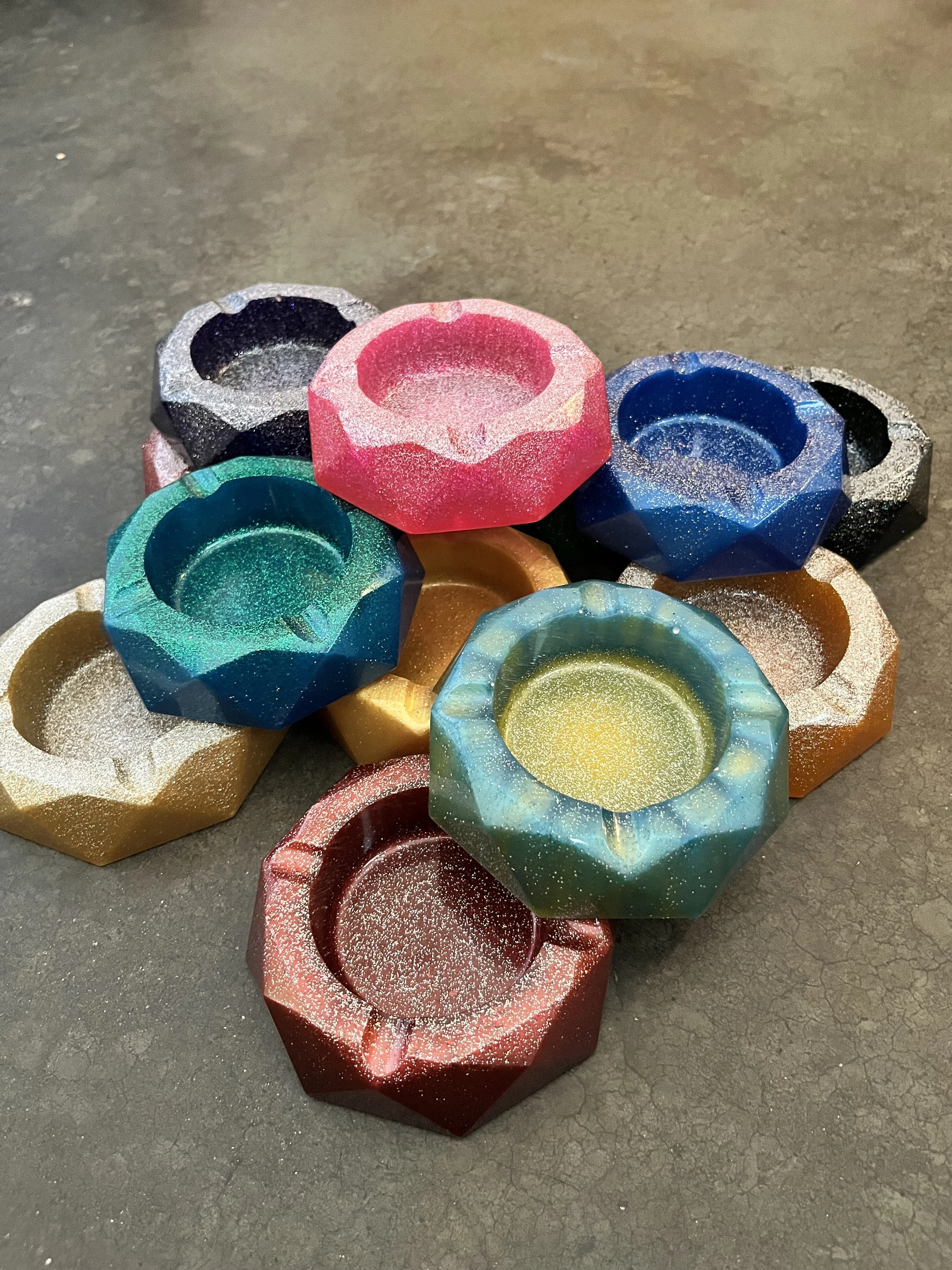 Colorful ash trays with a hexagonal shape and a star pattern inside, placed on a dark surface.