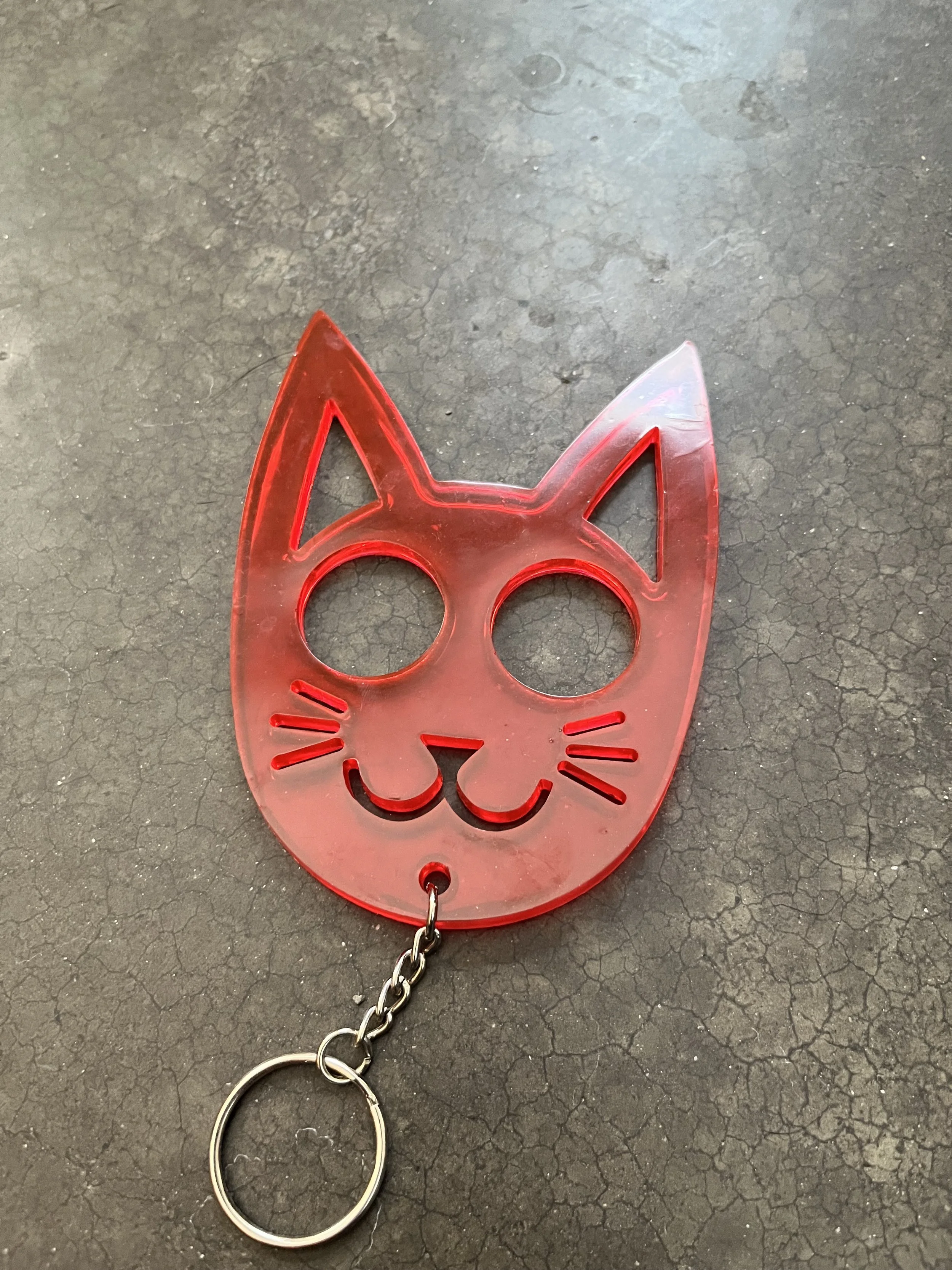 A red, cat-shaped emergency keychain, resting on a dark, textured surface.