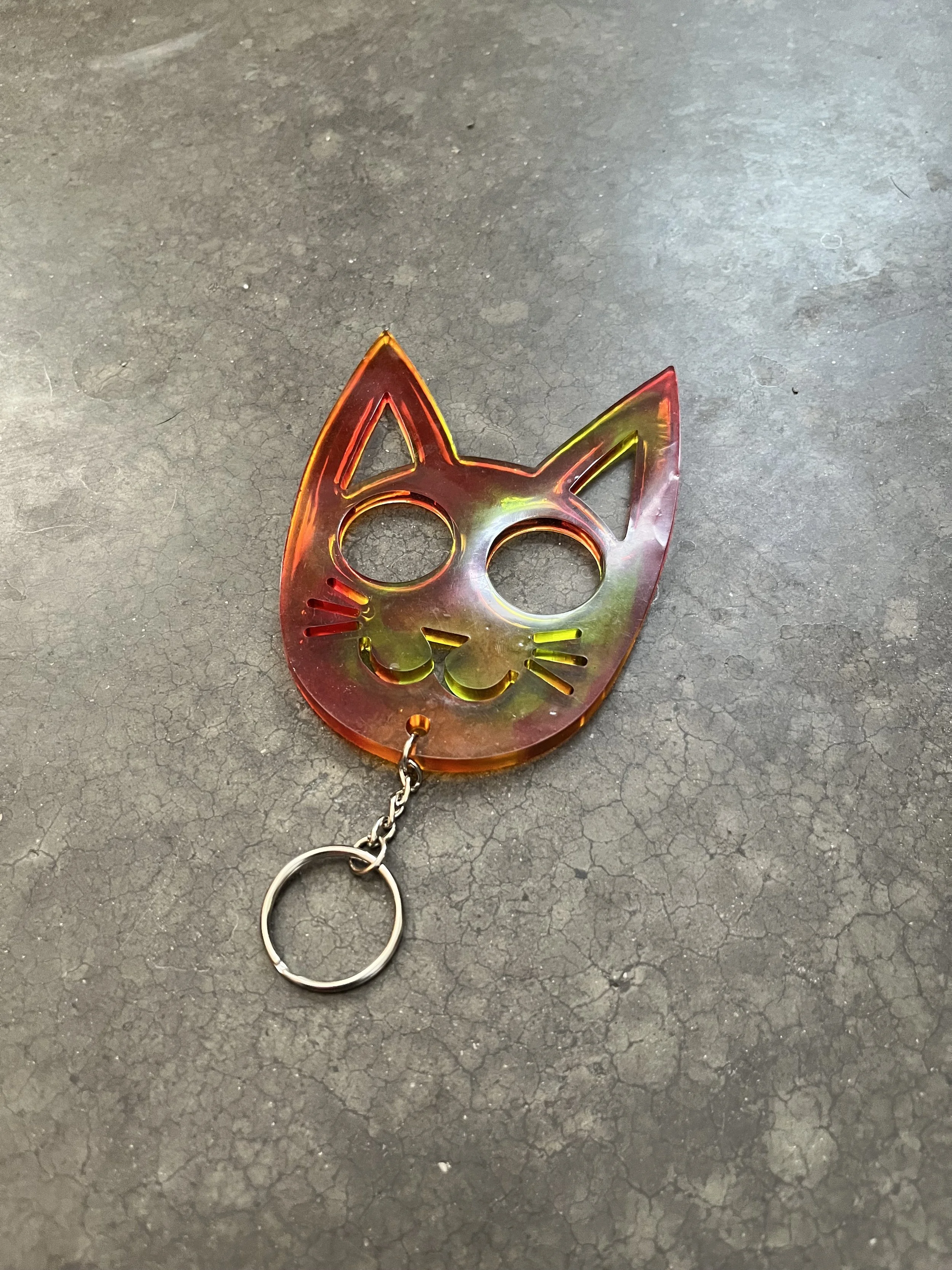 A keychain in the shape of a stylized cat's face with pointed ears and cut-out facial features, made of epoxy resin.