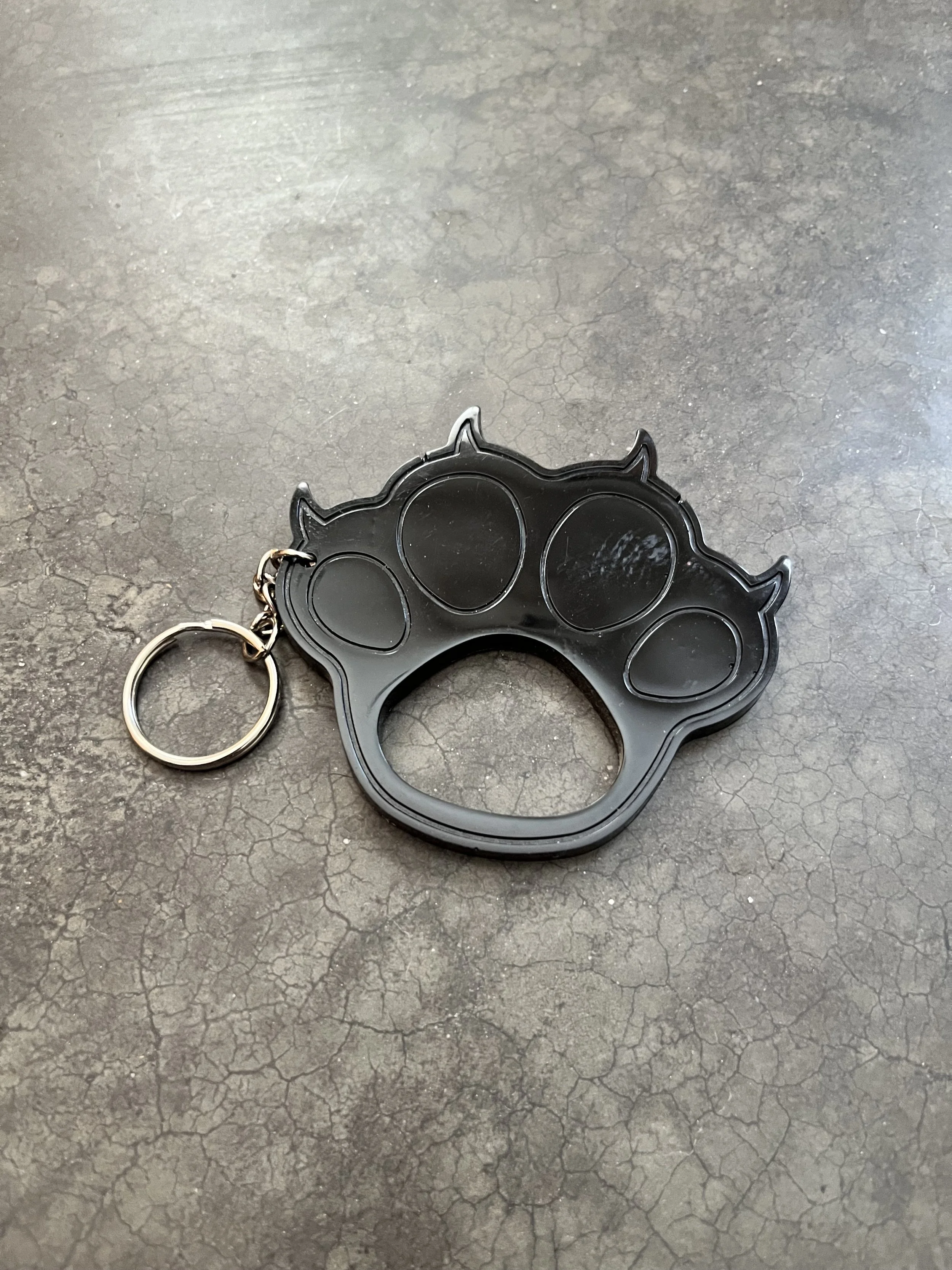 A black handmade epoxy resin emergency keychain kresting on a cracked gray surface.