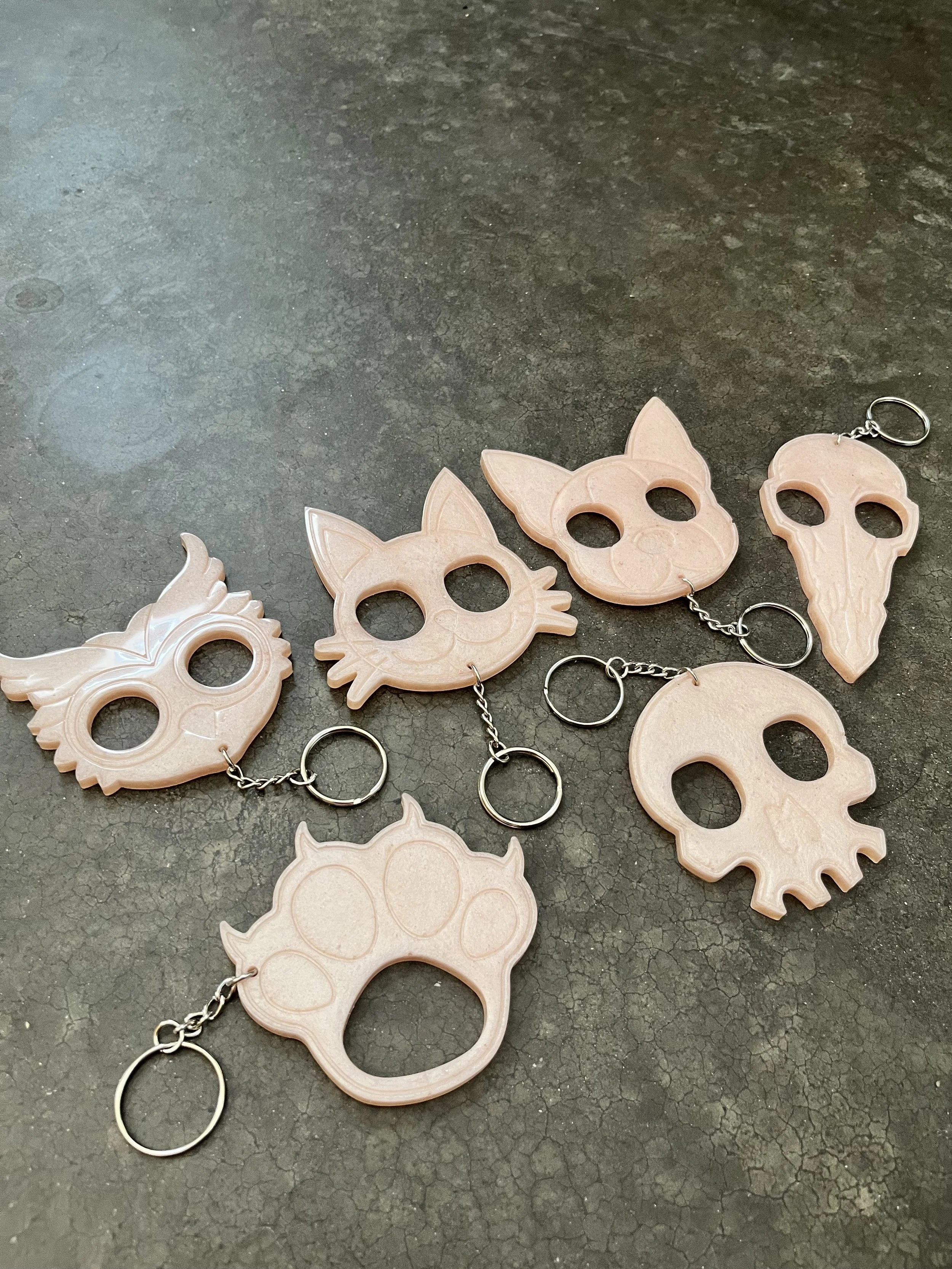 A keychain with multiple pink plastic skull-shaped charms, each with carved-out eye sockets and nose, connected by silver chains and rings, placed on a dark textured surface.