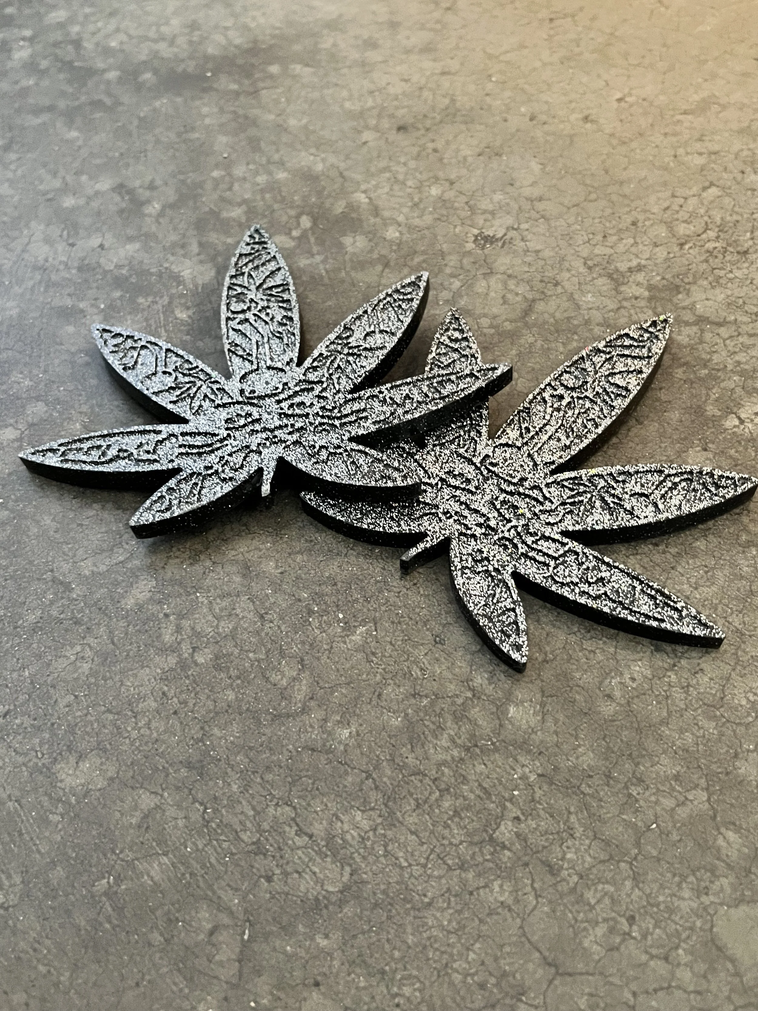 Silver glittery marijuana leaf coasters on a gray textured surface.