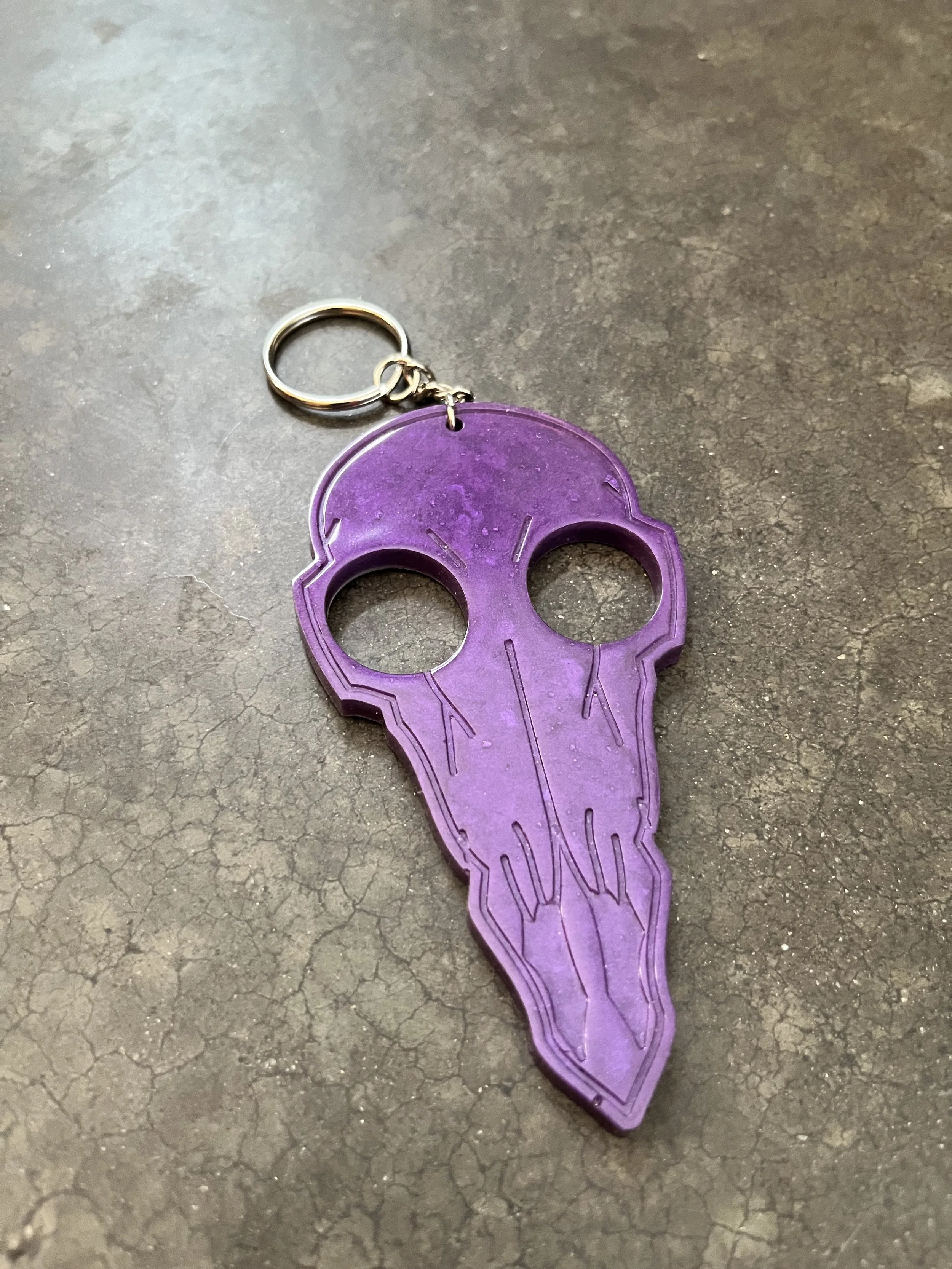 A handmade purple resin epoxy emergency keychain shaped like a birds skull.